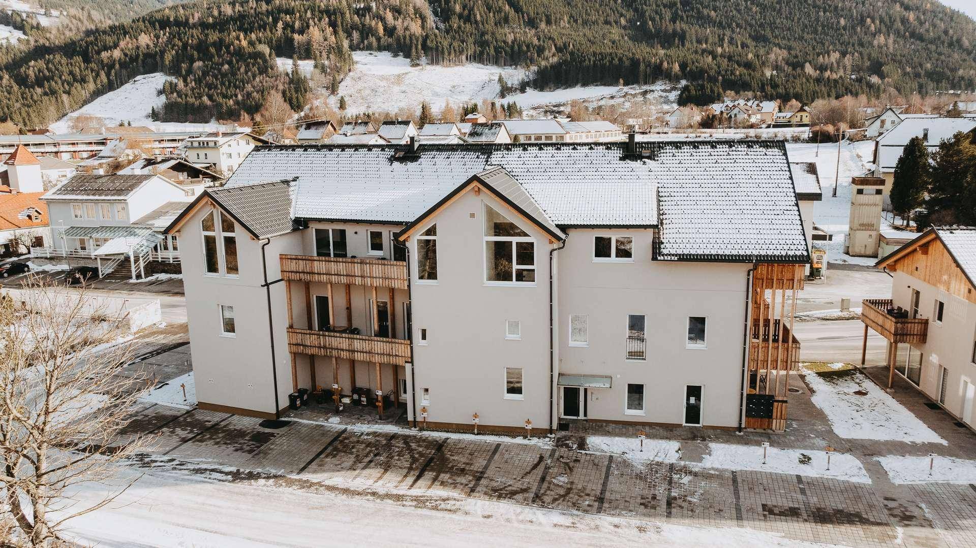 Ansicht des modernen Wohnkomplexes von hinten, umgeben von verschneiter Berglandschaft.