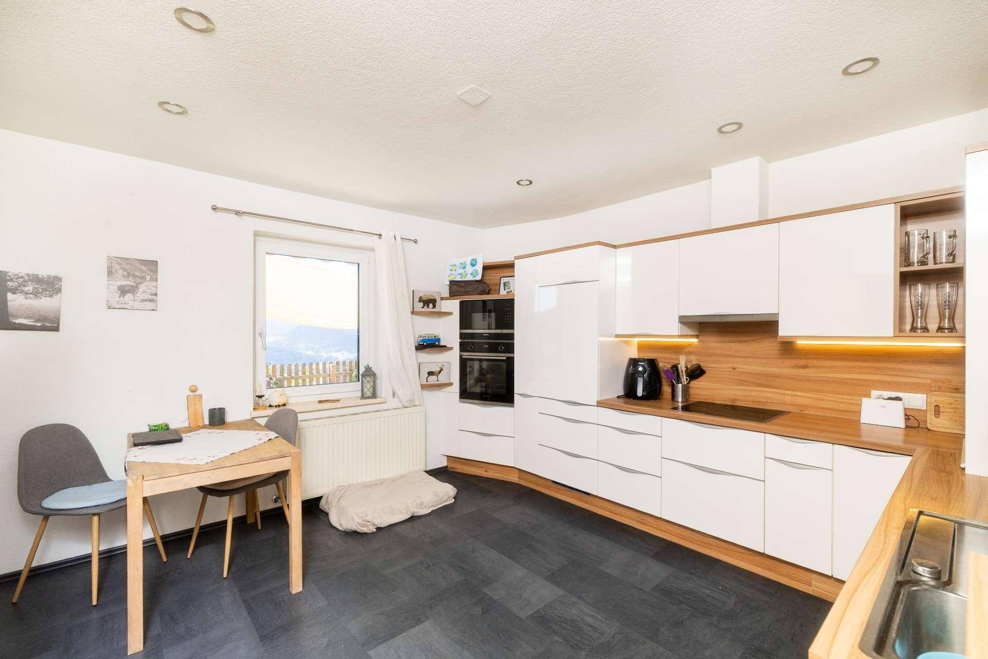 Gemütliche Wohnküche mit weißen Schränken, Holzarbeitsplatten und Essbereich am Fenster.
