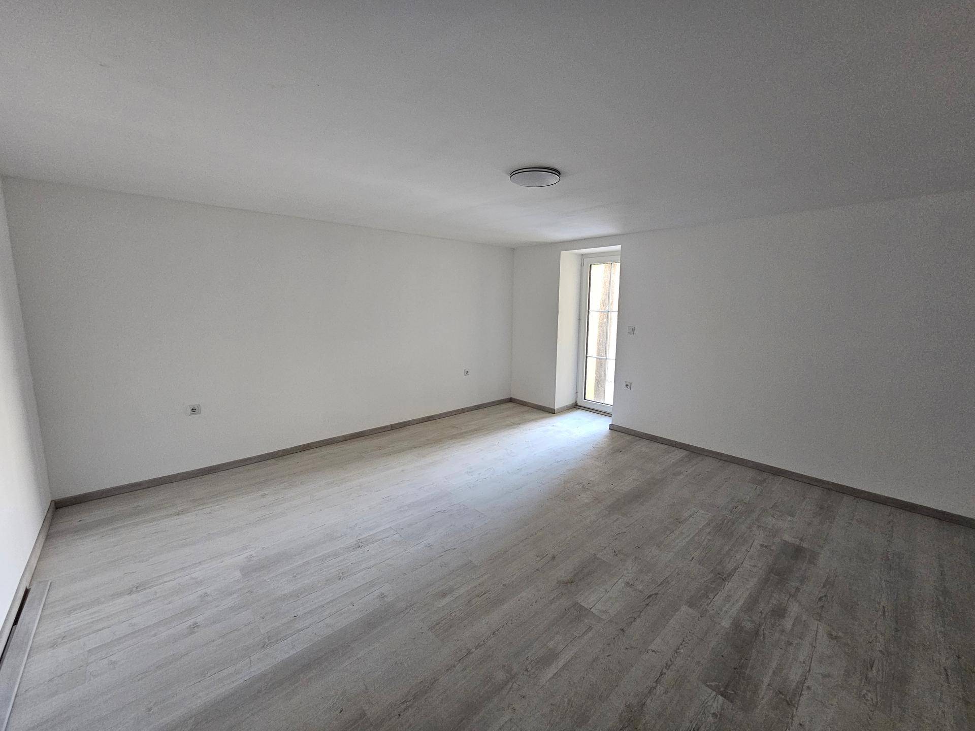 Lichtdurchfluteter Raum mit hellem Laminatboden und einer Tür, die ins Freie führt.