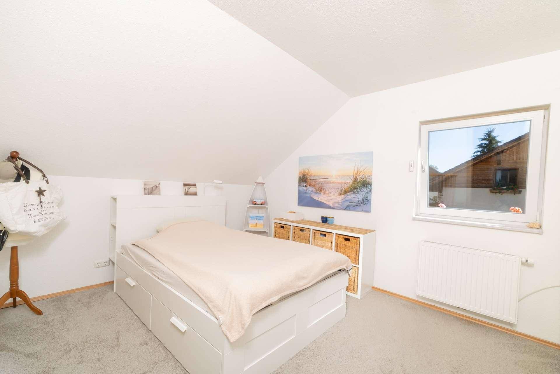 Helles Schlafzimmer mit Doppelbett, Teppichboden und Dachschräge für gemütliche Atmosphäre.