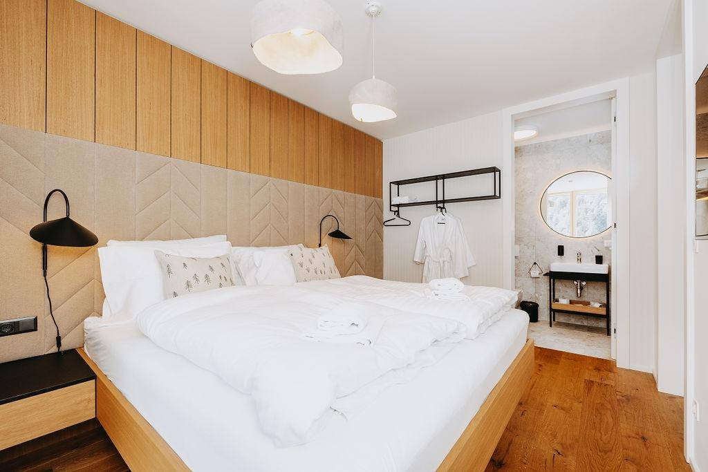 Gemütliches Schlafzimmer mit Holzboden, gepolstertem Kopfteil und direktem Zugang zum Badezimmer.