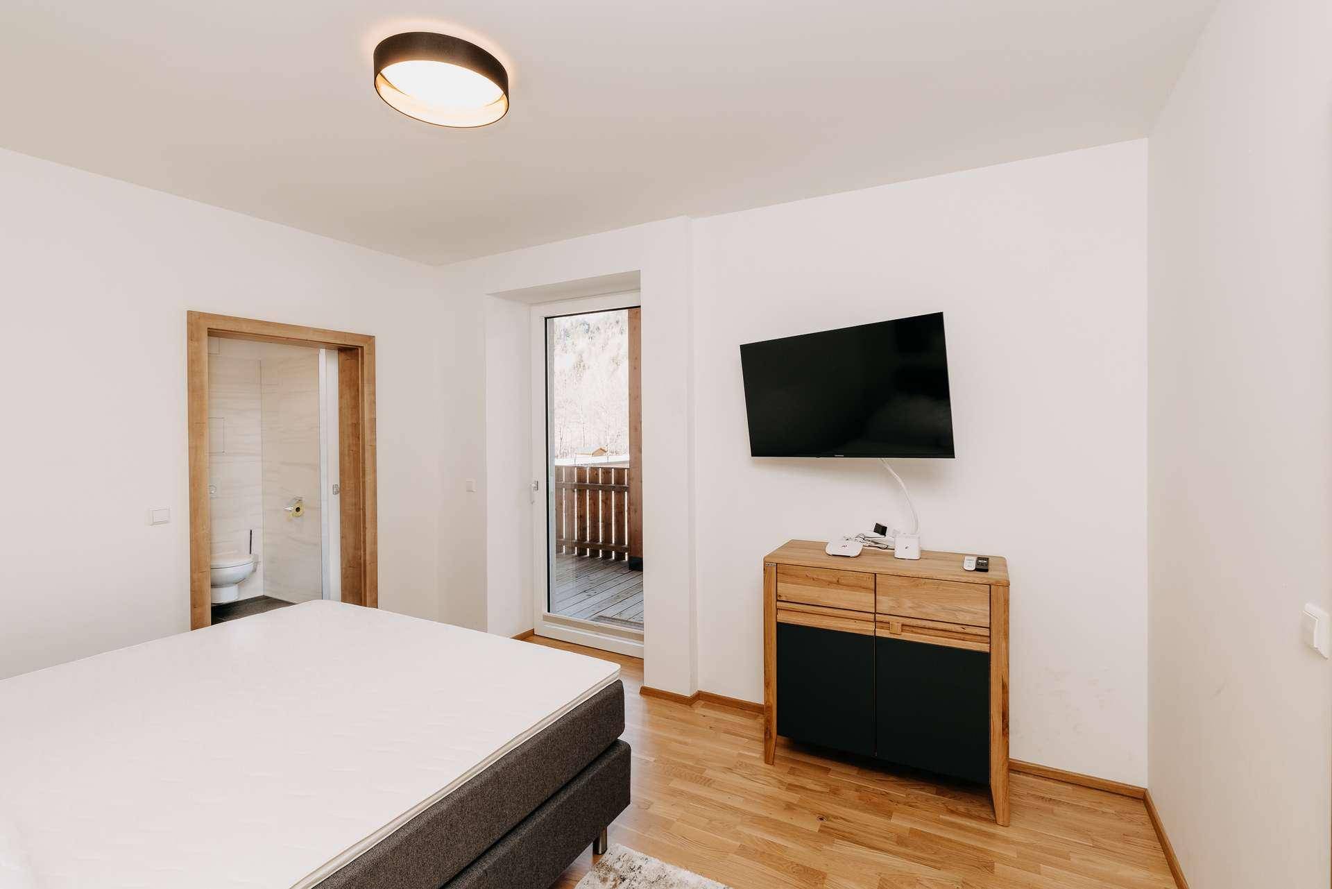 Schlafzimmer mit Holzboden, Wand-TV und direktem Zugang zu einem Balkon.