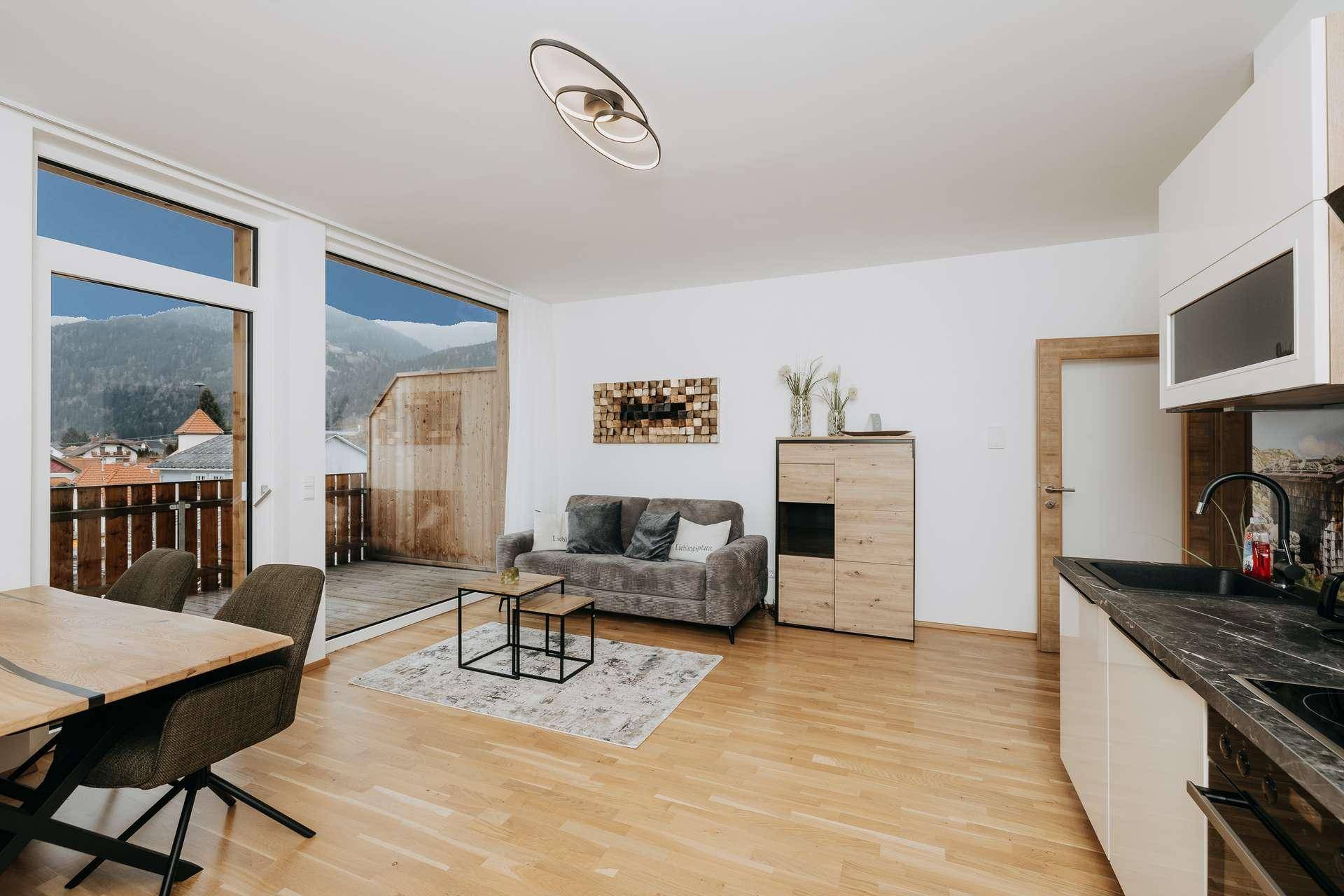 Heller Wohnbereich mit Sofa, Zugang zum Balkon und integrierter Küche, bietet einen weiten Ausblick.
