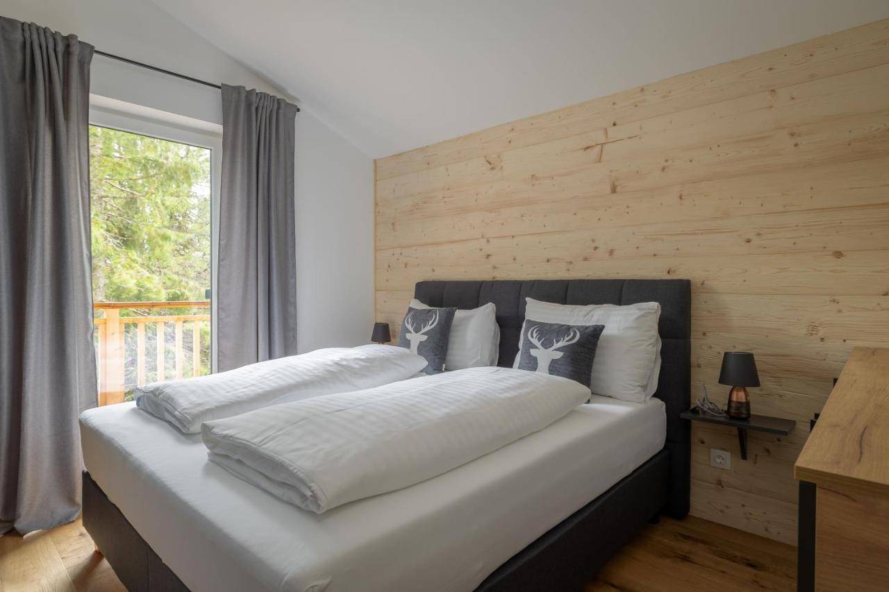 Helles Schlafzimmer mit Holzwand, Doppelbett und Blick ins Grüne.