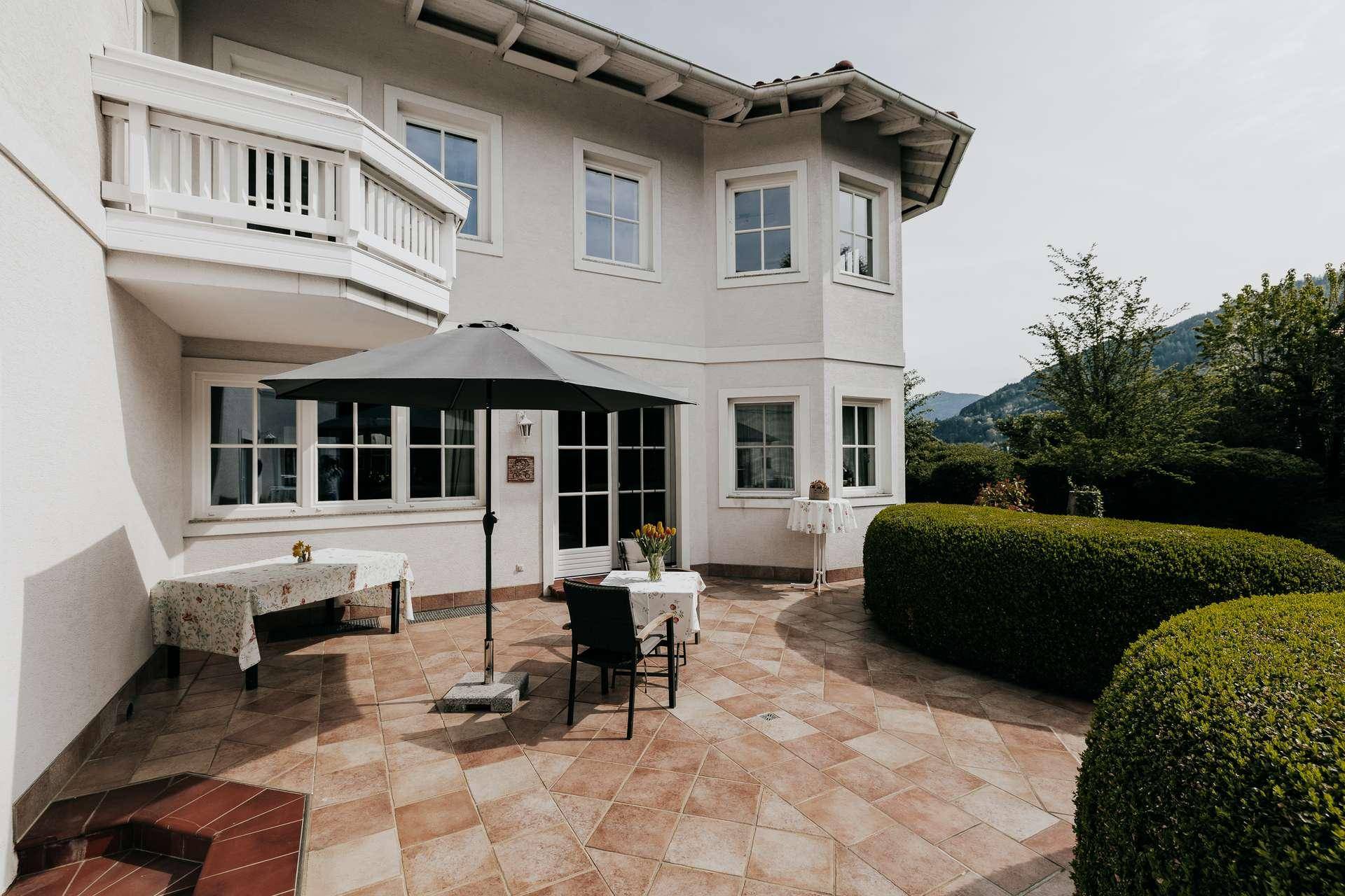 Gemütliche Terrasse mit Fliesenboden, Sonnenschirm und Blick auf die umliegende Berglandschaft.