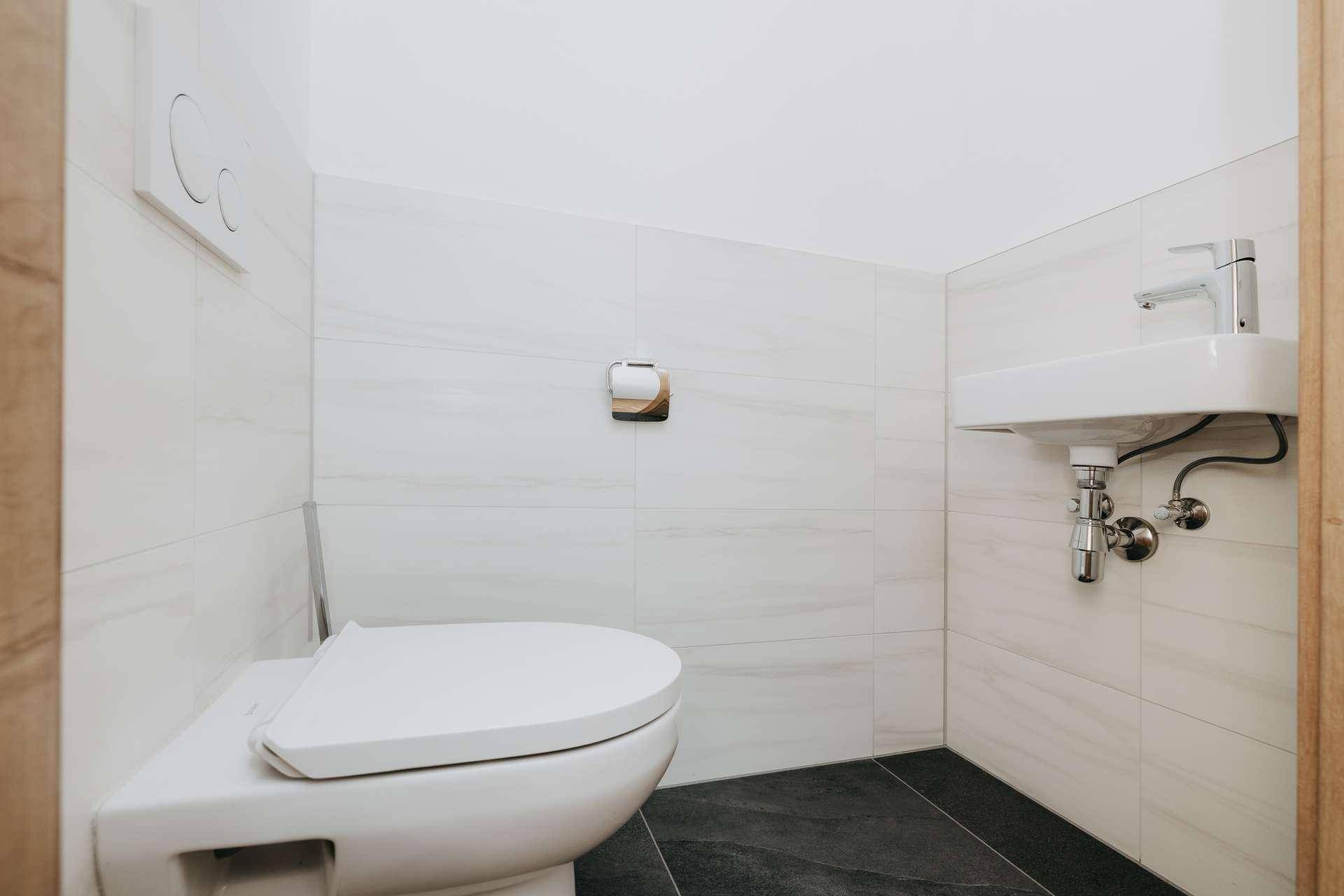 Helles Gäste-WC mit wandhängender Toilette und kleinem Waschbecken, modern gefliest.