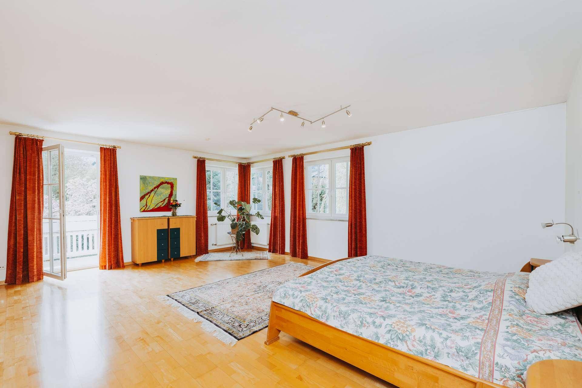 Helles Schlafzimmer mit Holzboden, Zugang zum Balkon und Blick ins Grüne.