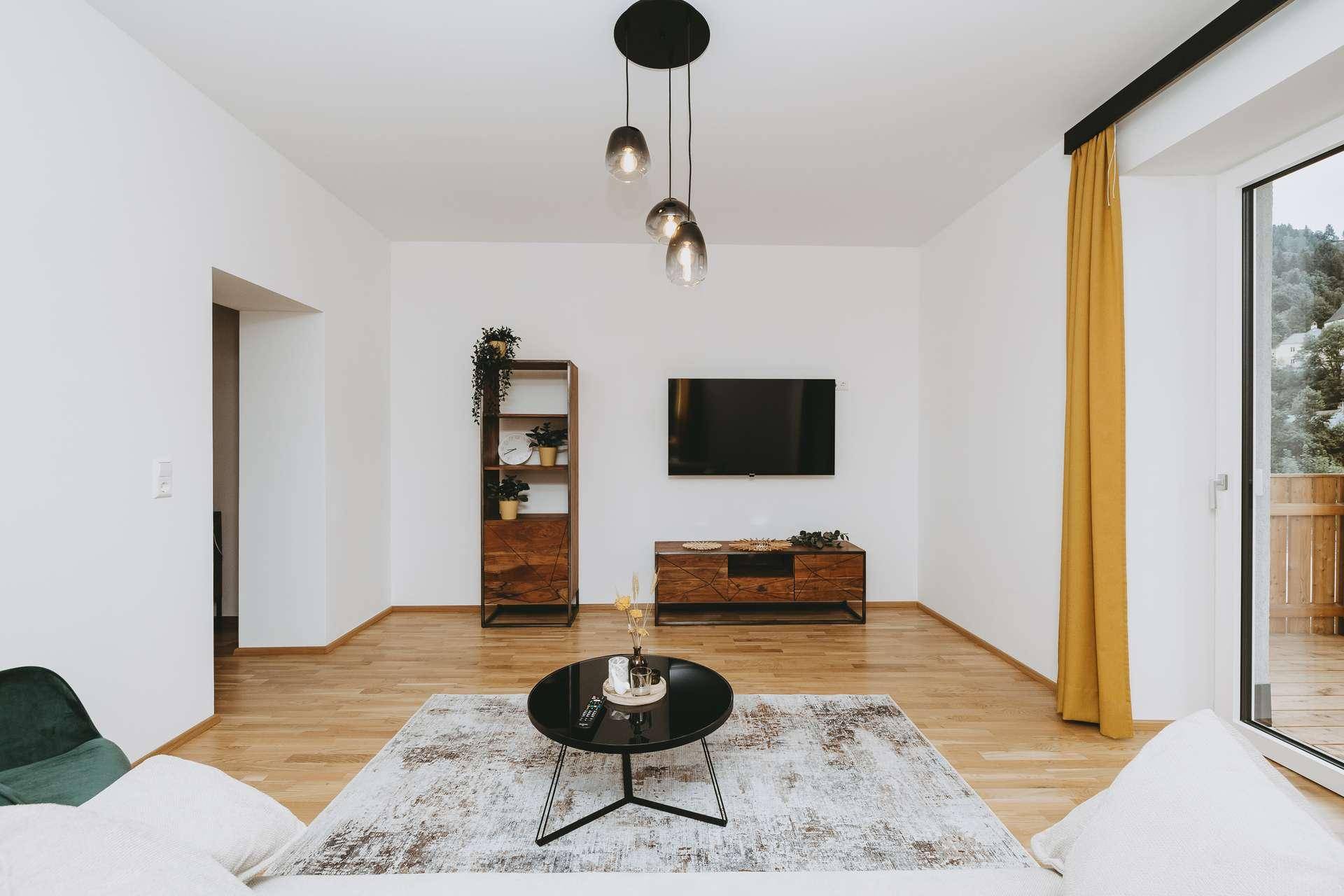 Geräumiges Wohnzimmer mit Holzboden, TV-Bereich und Blick auf die umliegende Natur.