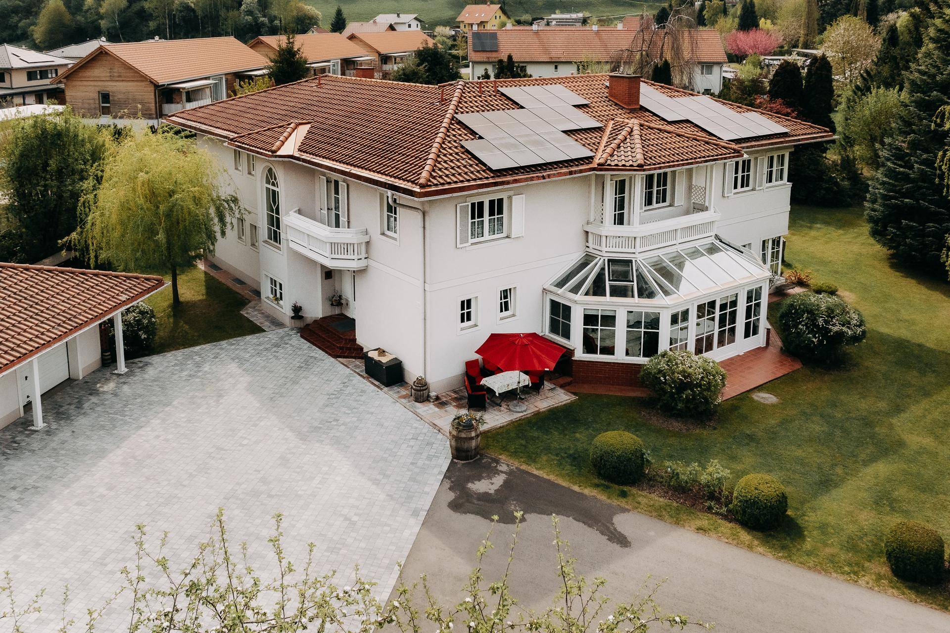 Gesamtansicht des Hauses mit Wintergarten, Garage und gepflasterter Auffahrt in ländlicher Umgebung.