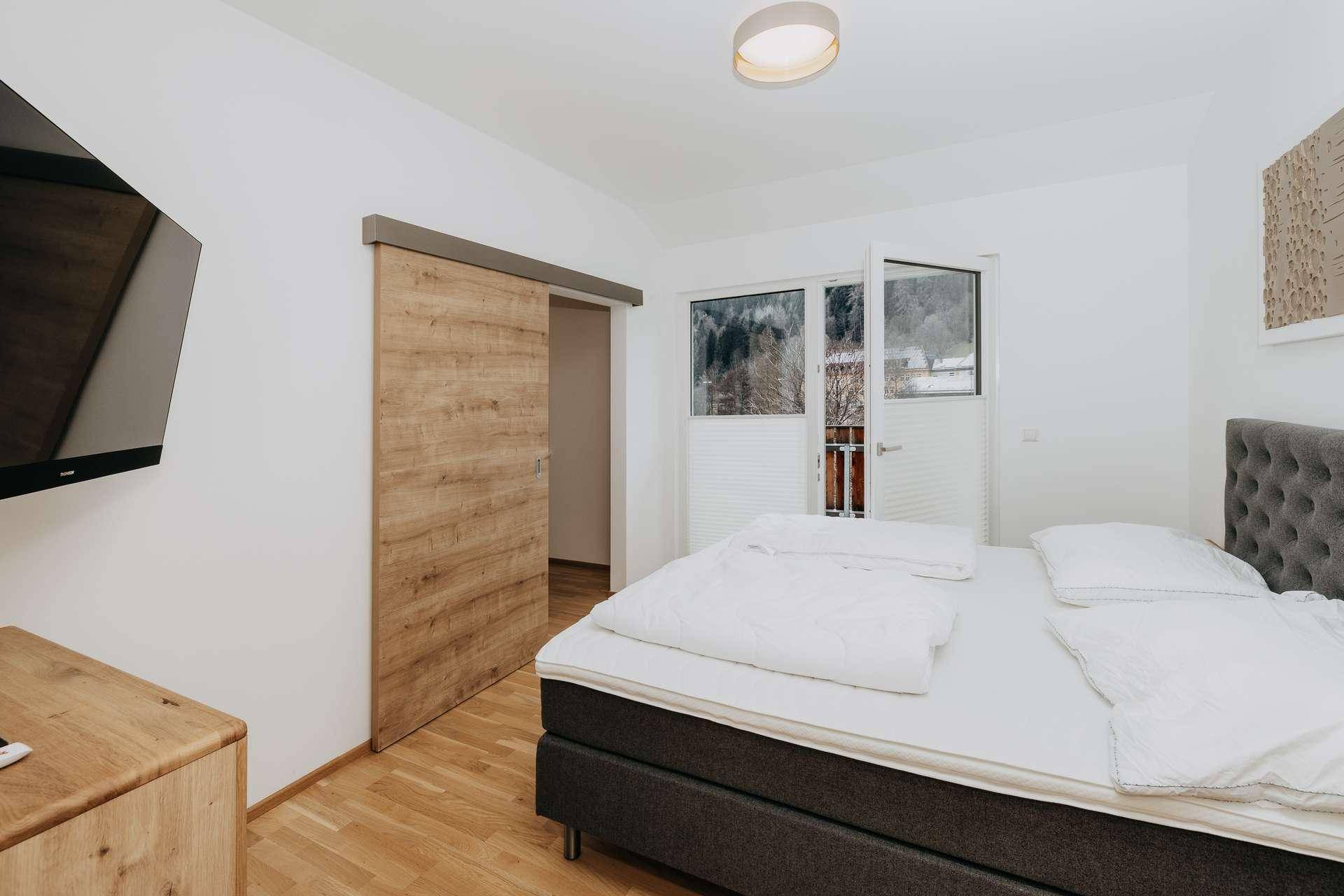 Gemütliches Schlafzimmer mit Doppelbett, Holzboden und Schiebetür, bietet einen ruhigen Blick ins Grüne.