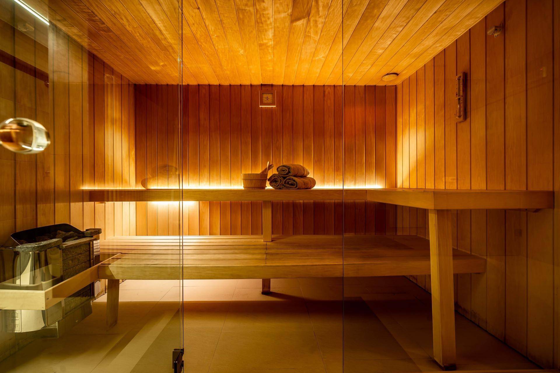 Innenansicht einer modernen Saunakabine aus Holz mit Bänken und einem Saunaofen.