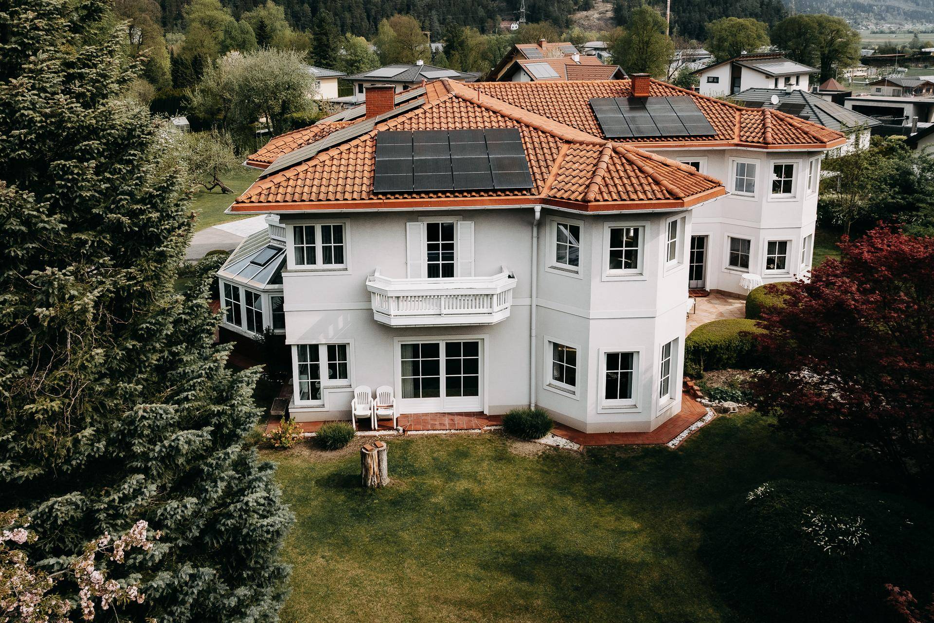 Seitenansicht des Hauses mit Wintergarten, Balkonen und Photovoltaikmodulen auf dem Ziegeldach.