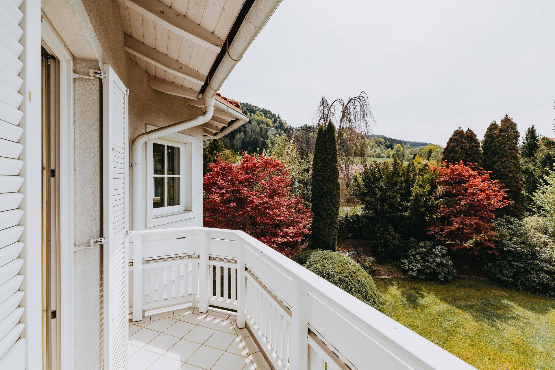Kleiner Balkon mit weißem Geländer und Blick auf die grüne Landschaft und Berge.