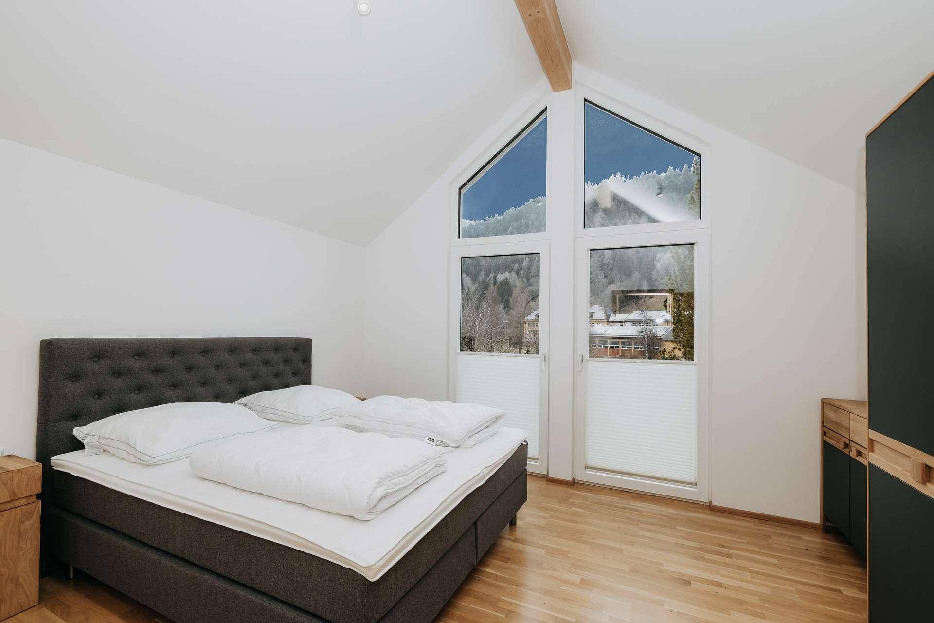 Helles Schlafzimmer mit Doppelbett, Holzboden und großen Fenstern, die einen beeindruckenden Bergblick bieten.