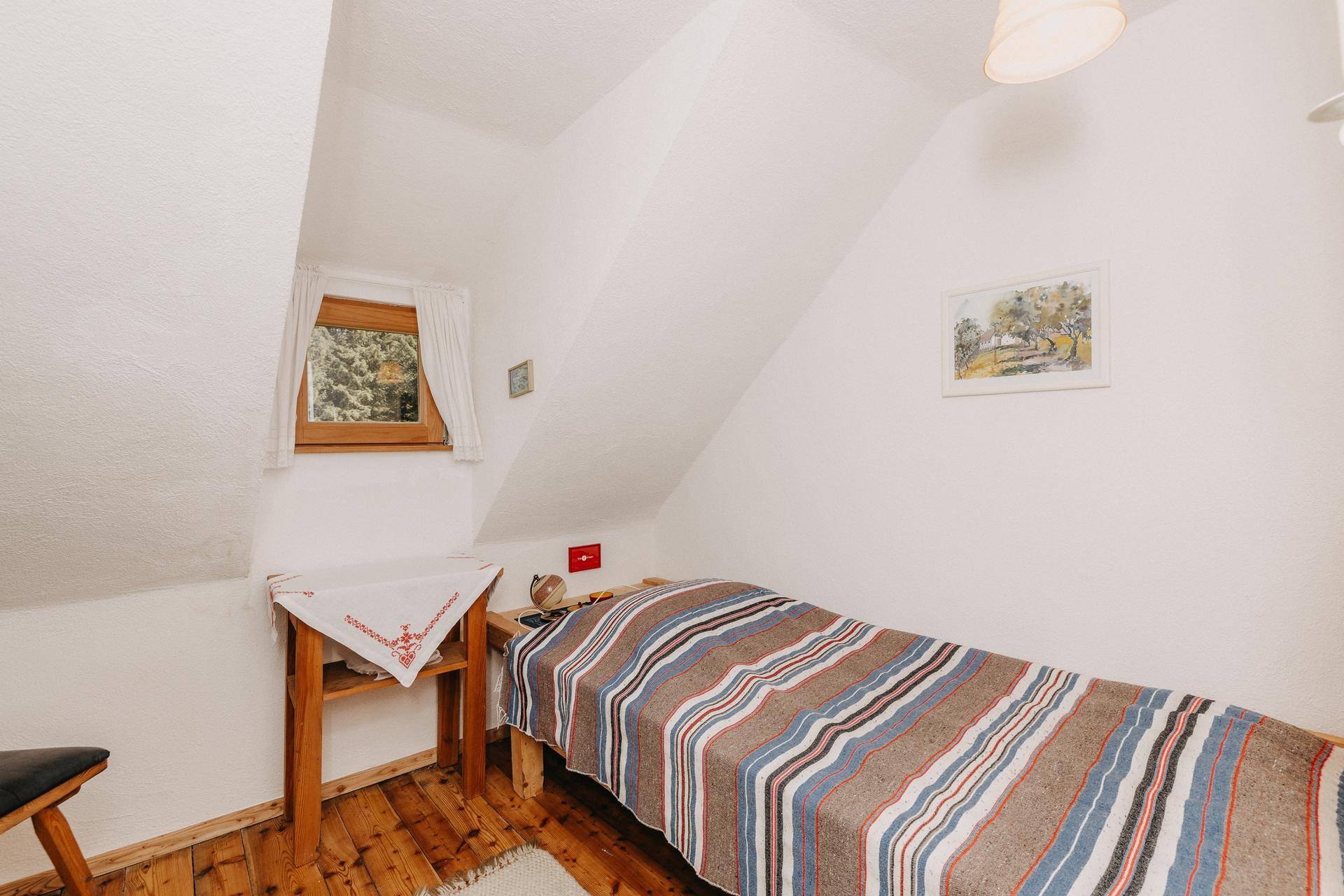 Kleines Schlafzimmer mit Einzelbett, Holzboden und Dachschräge.