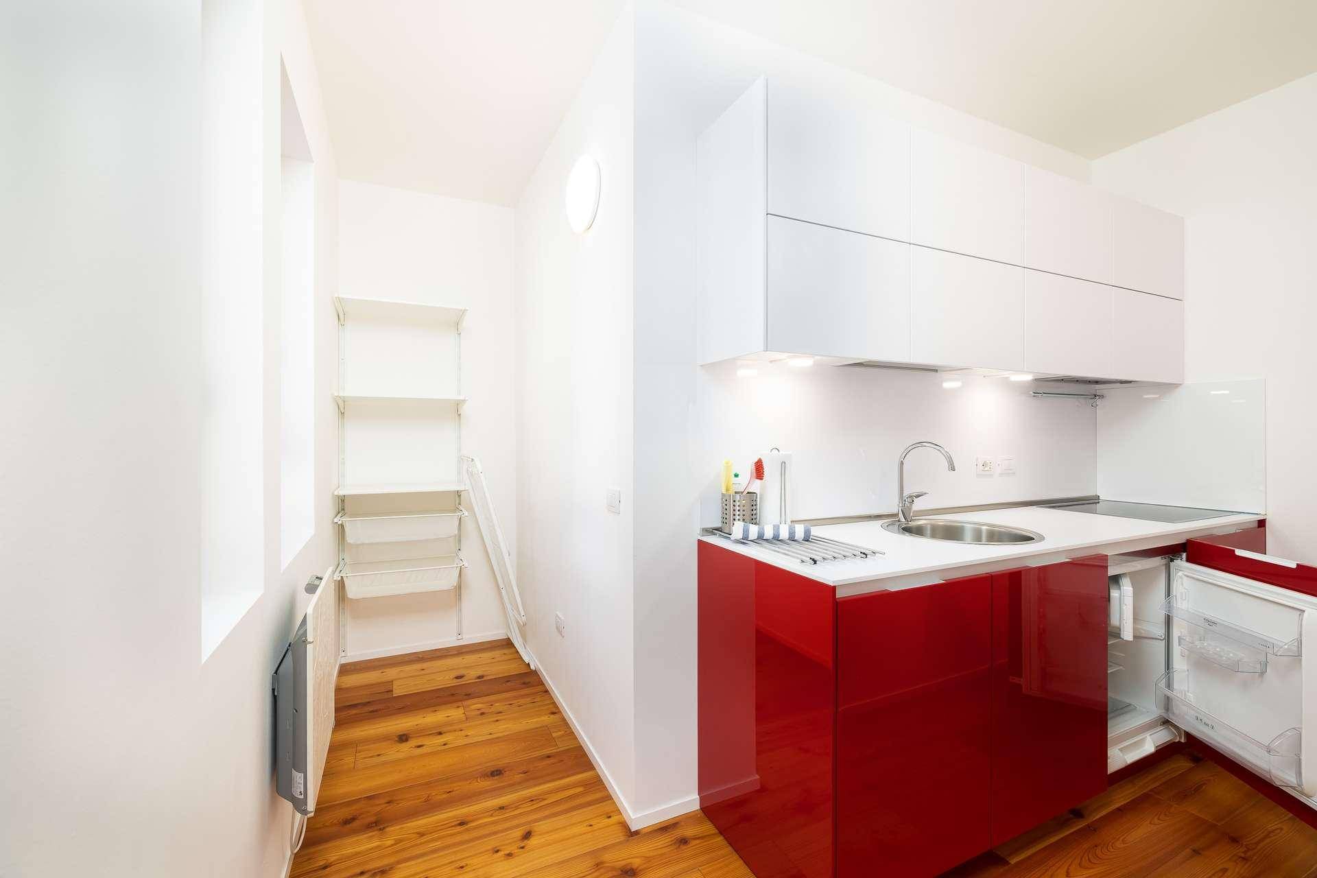 Moderne Küchenzeile mit roten Hochglanzfronten, Spüle und integriertem Kühlschrank in hellem Raum.