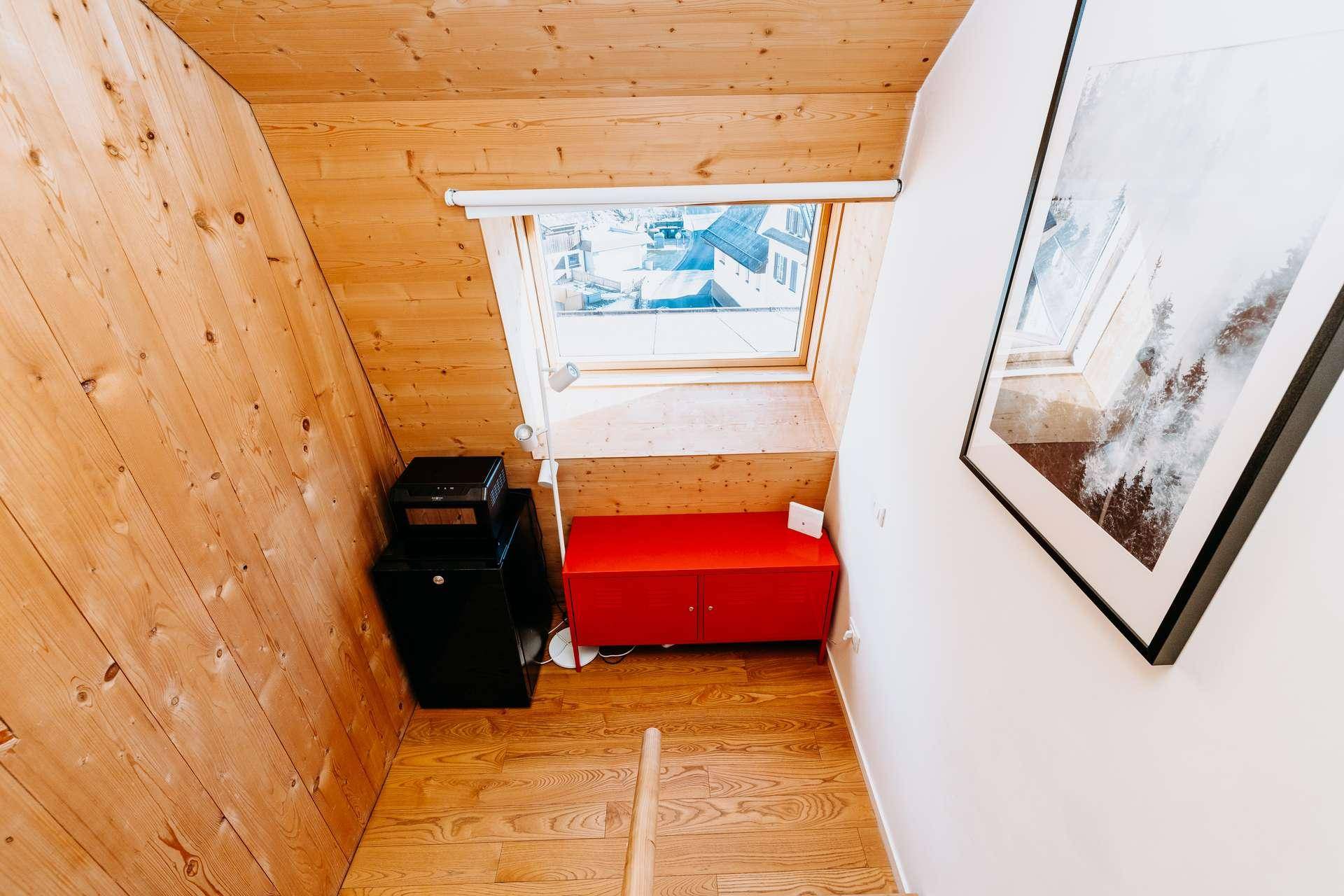 Helle Dachschräge mit Dachfenster, Holzboden und rotem Sideboard.