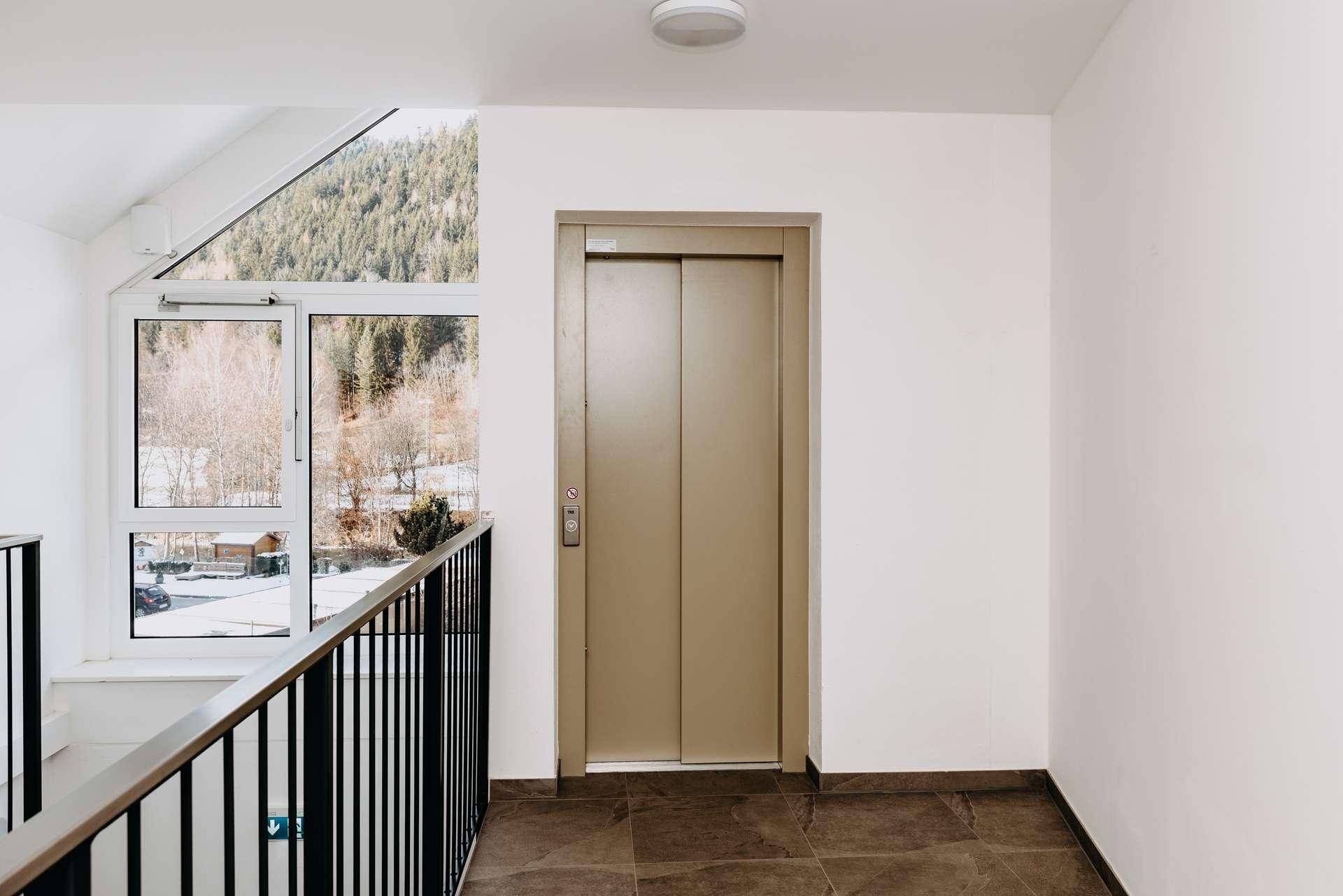 Heller Treppenhausbereich mit Aufzug und großem Fenster mit Blick auf die Berge.
