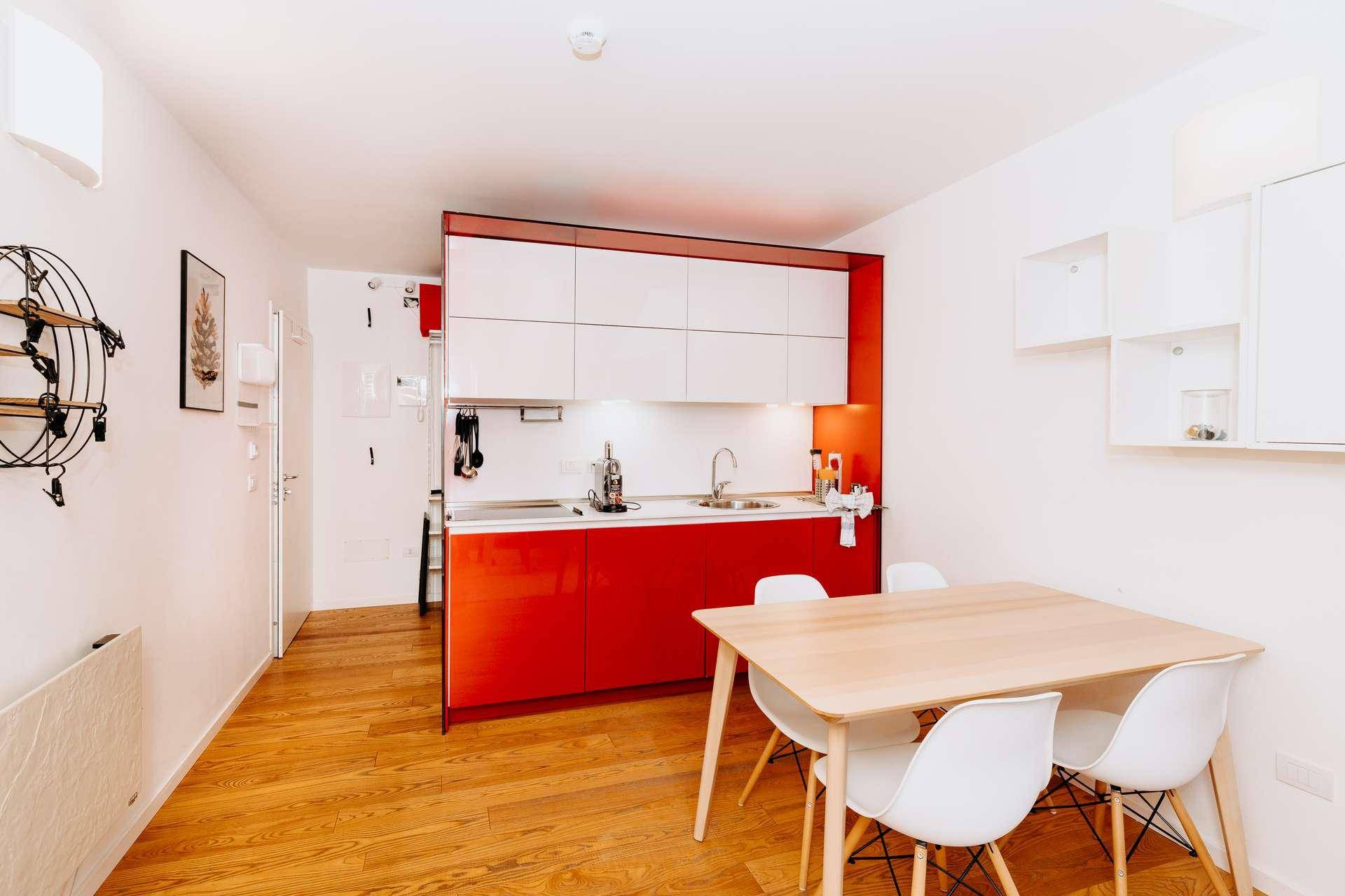 Moderne Küche mit roten Hochglanzfronten, Holzboden und Essbereich.