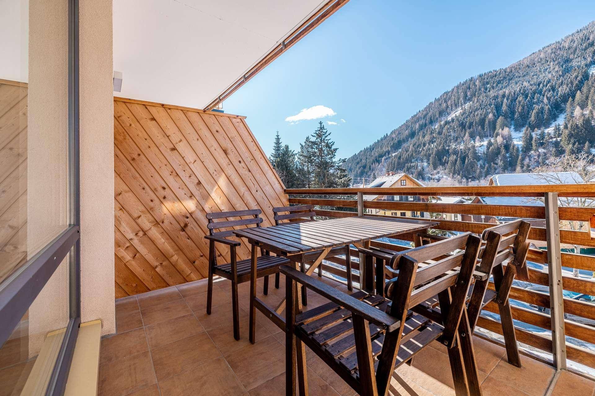 Geräumiger Balkon mit Holztisch und Stühlen, umgeben von einer winterlichen Berglandschaft.