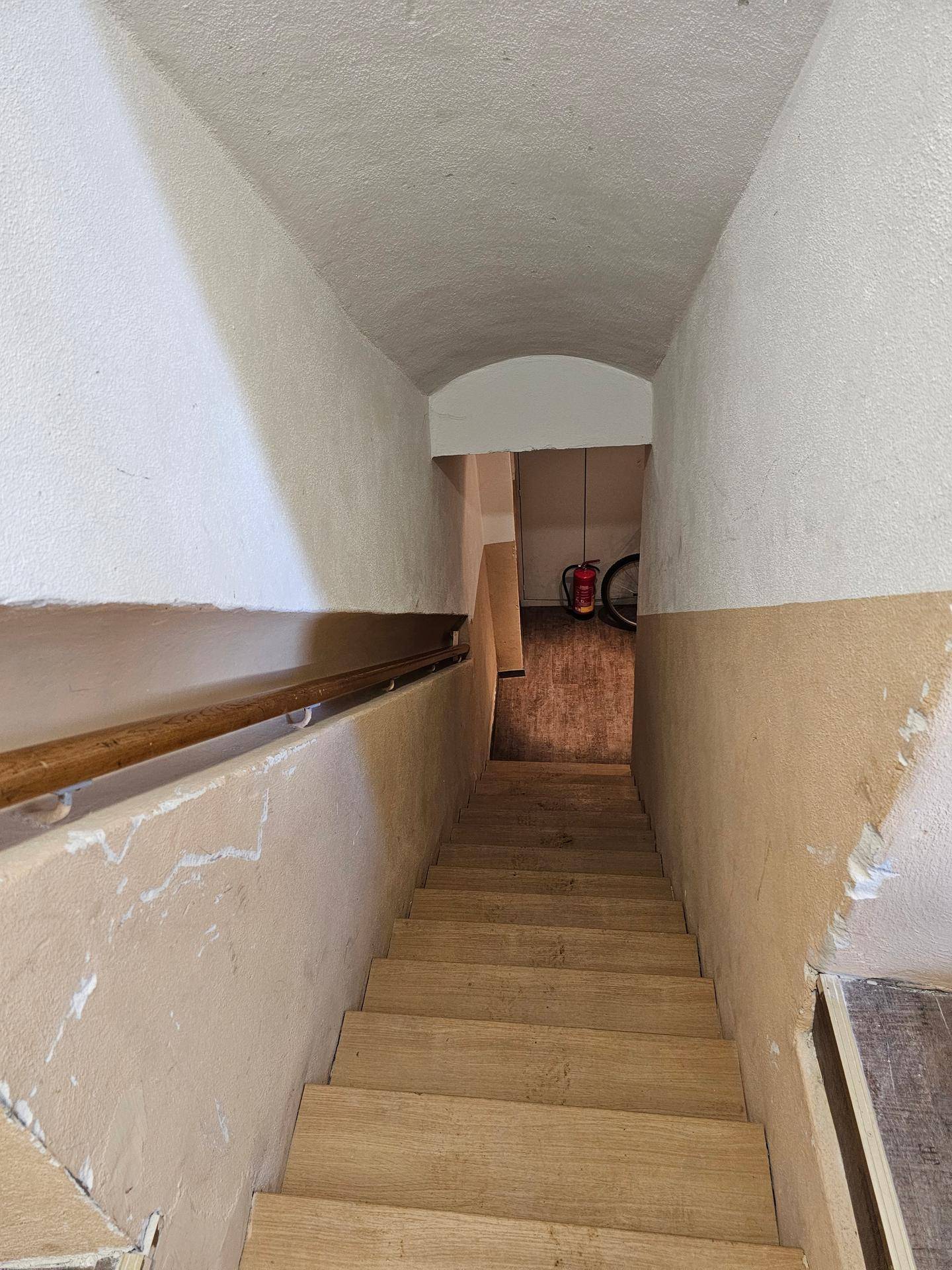 Holztreppe mit Handlauf in einem Flur mit gewölbter Decke und zweifarbigen Wänden.