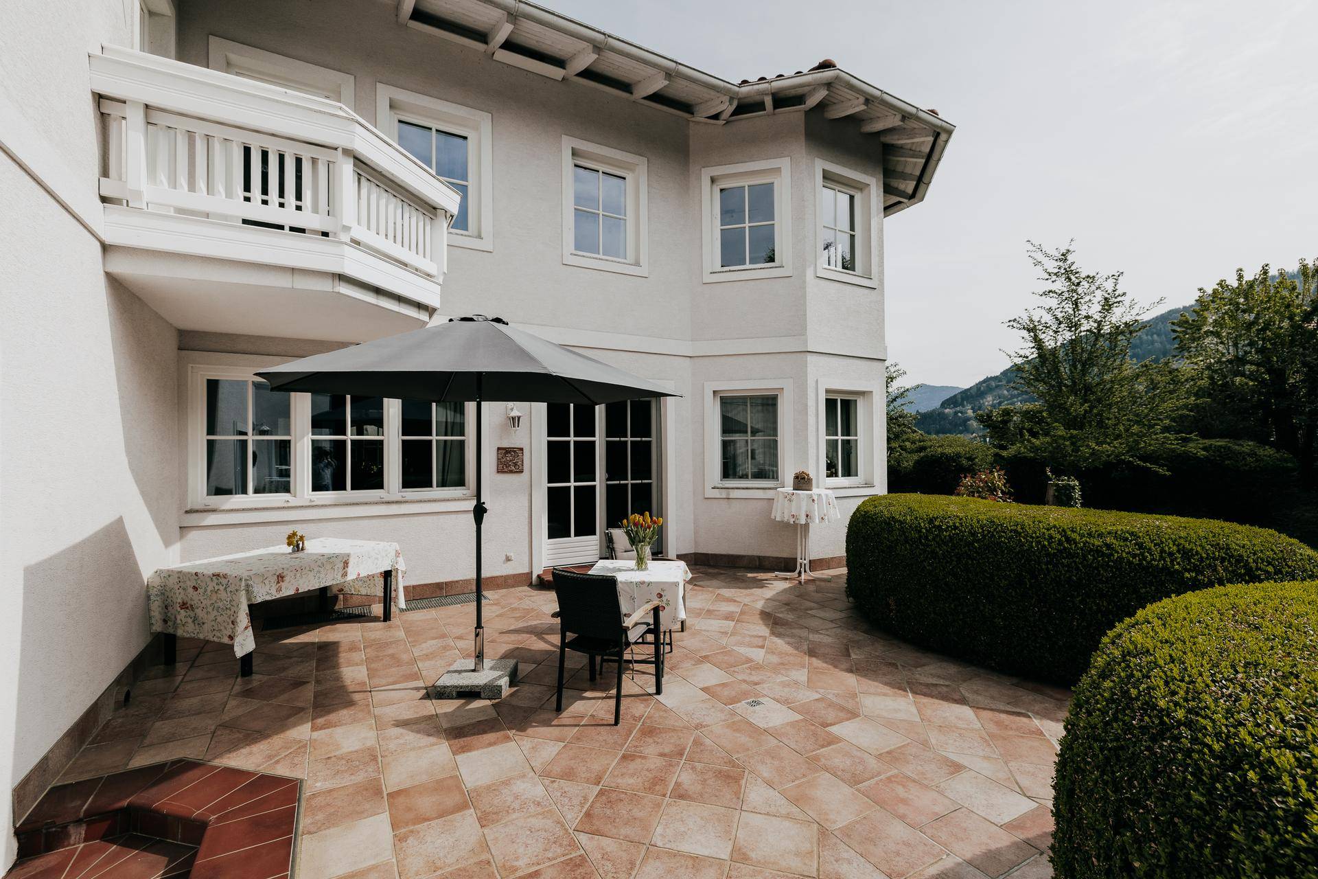 Geflieste Terrasse mit Gartenmöbeln und Sonnenschirm, ideal für Mahlzeiten im Freien.