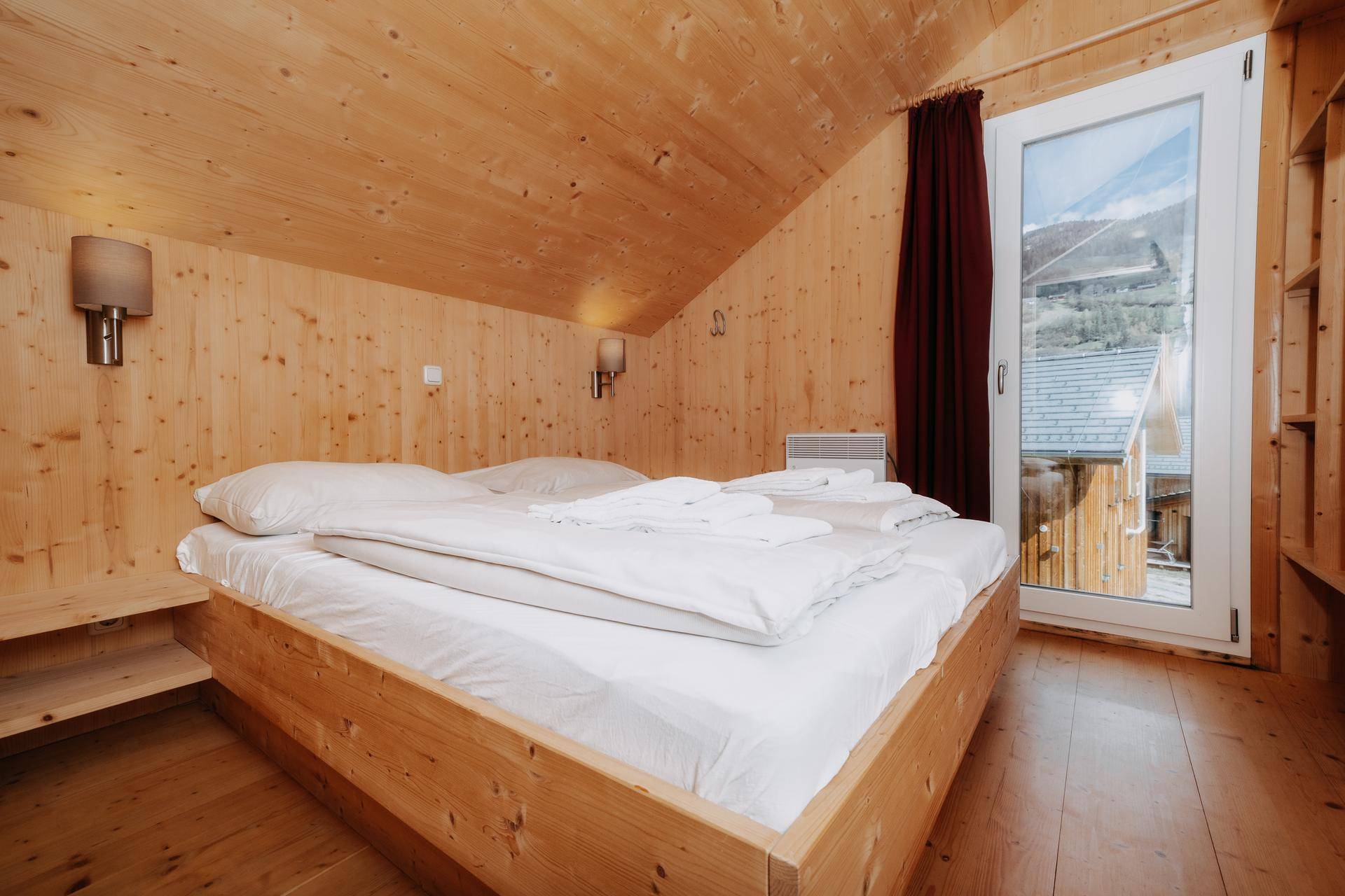 Komfortables Schlafzimmer mit Holzbett, schrägen Wänden und Zugang zu einem Balkon.