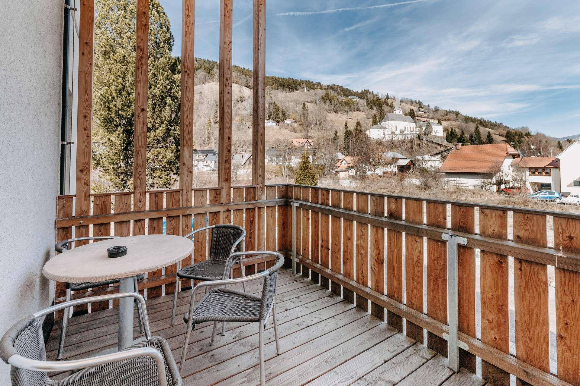 Sonniger Holzbalkon mit Sitzgelegenheiten und weitem Blick auf die Berglandschaft.