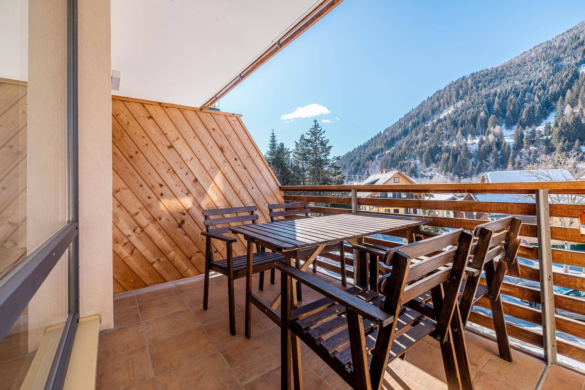Geräumiger Balkon mit Holztisch und Stühlen, umgeben von Holzverkleidung und Bergblick.