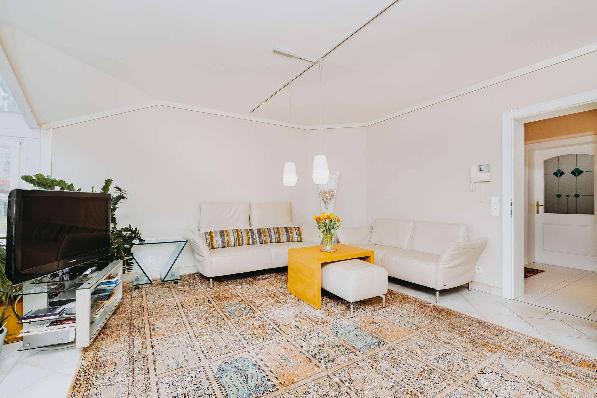 Helles Wohnzimmer mit beigen Sofas, großem Teppich und Zugang zu einem weiteren Raum.