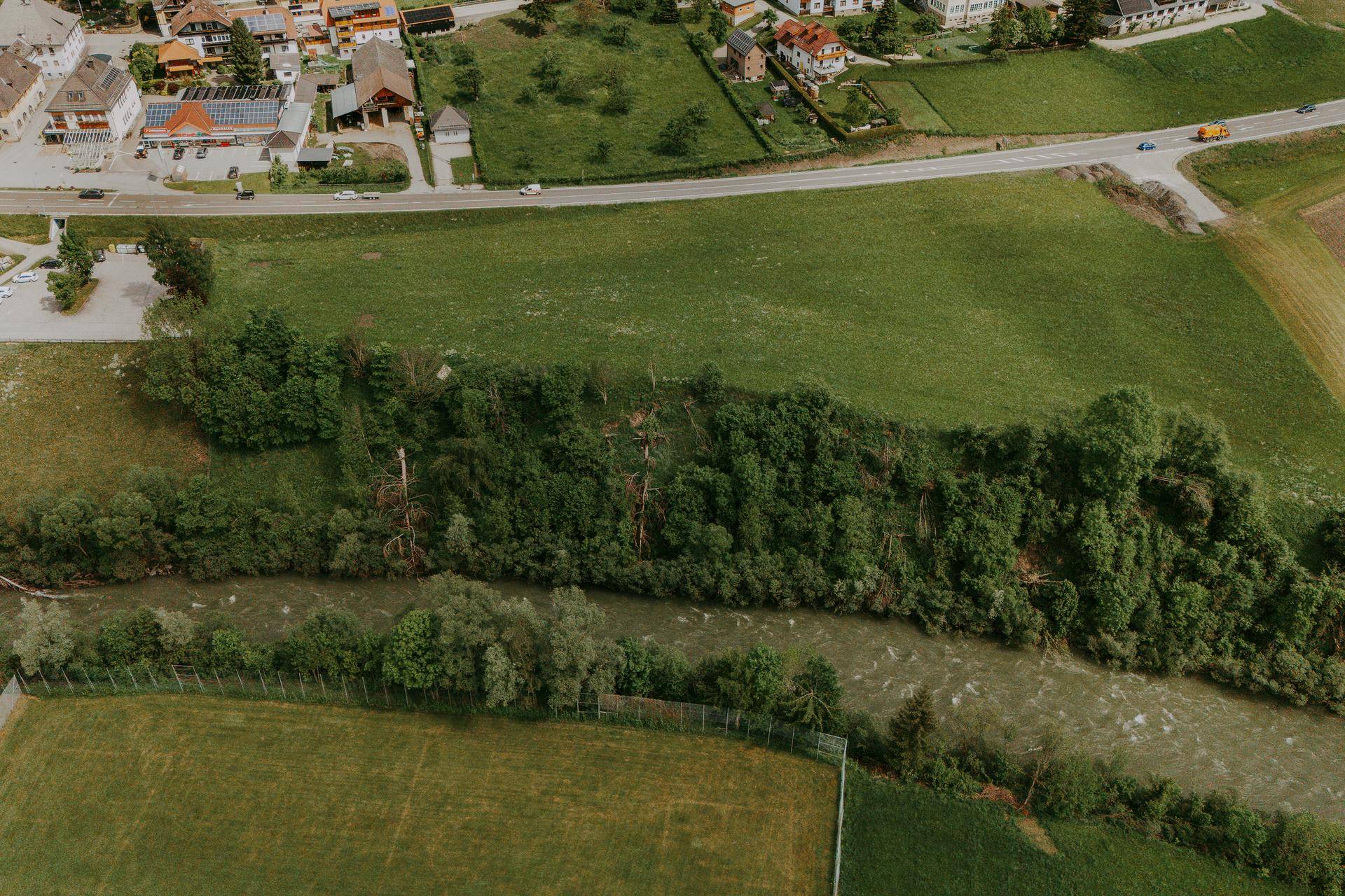 Nahaufnahme aus der Vogelperspektive eines Flusses, der sich durch eine grüne Landschaft mit Bäumen und Feldern schlängelt.