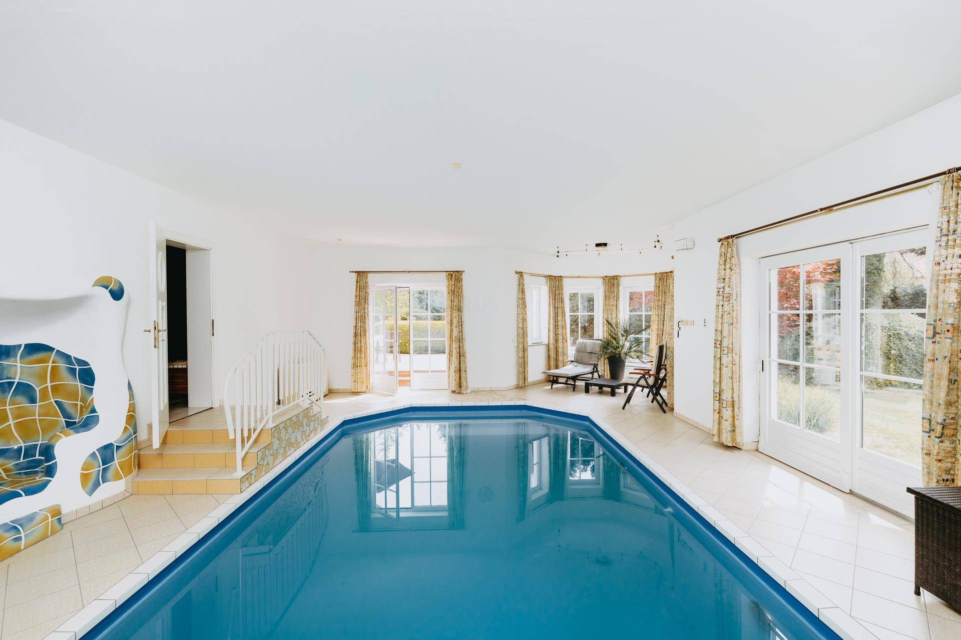 Innenpoolbereich mit großem Schwimmbecken, Fliesenboden und Zugang zum Garten.