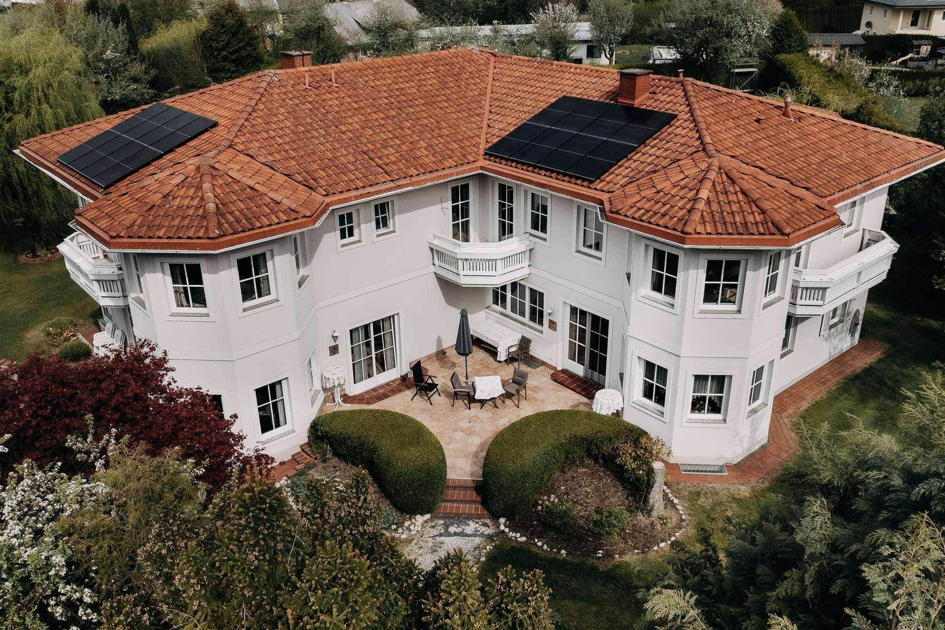 Rückseite des Hauses mit großer gefliester Terrasse, Sitzgelegenheiten und gepflegten Hecken.