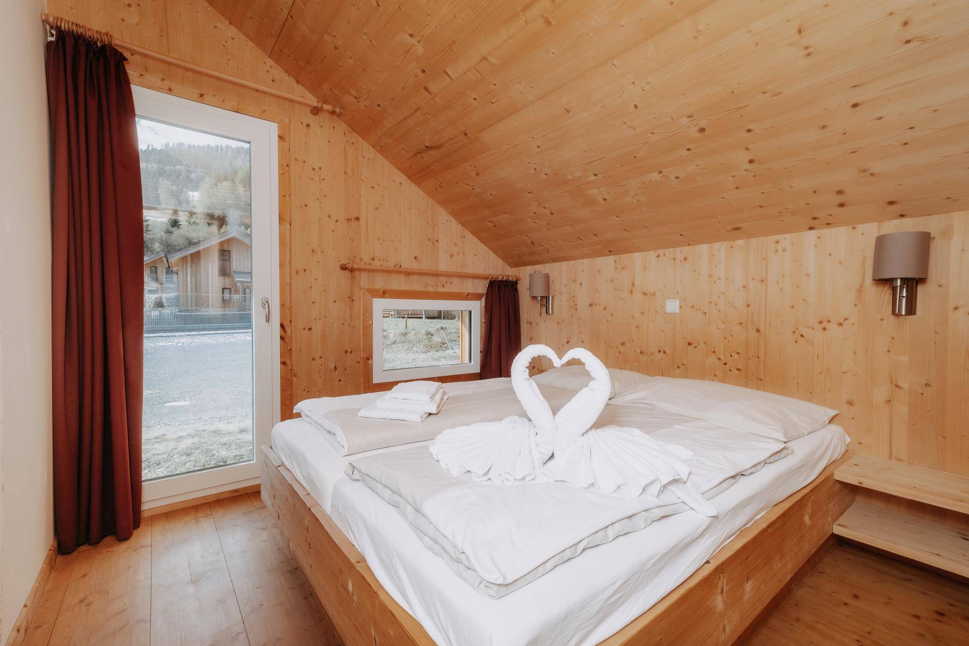 Gemütliches Schlafzimmer mit Holzwänden und -decke, Doppelbett und großem Fenster.