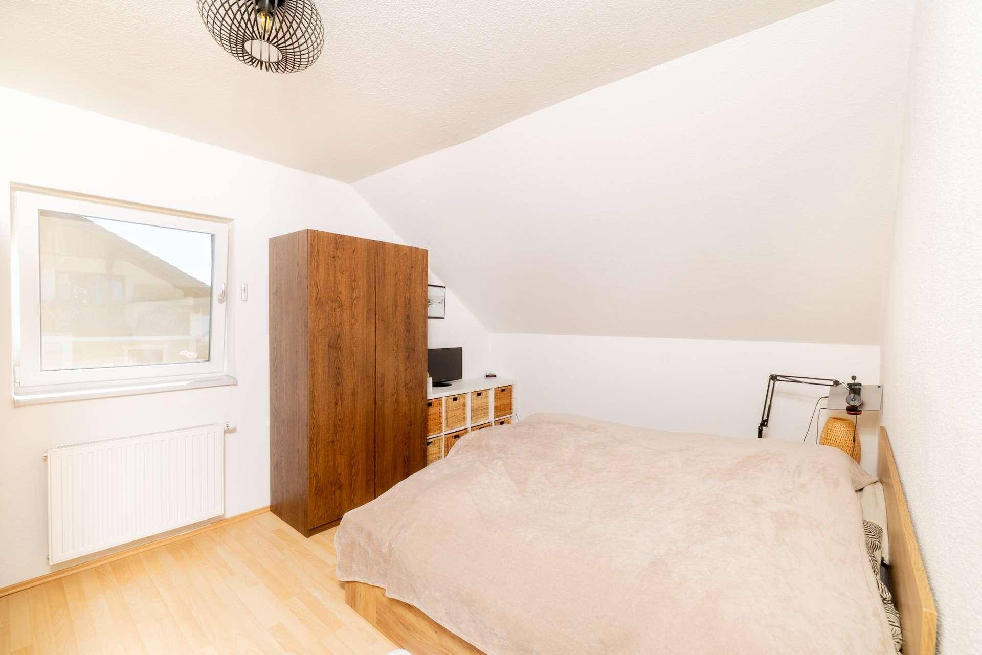 Schlafzimmer mit Doppelbett, Holzschrank und Laminatboden unter einer Dachschräge.