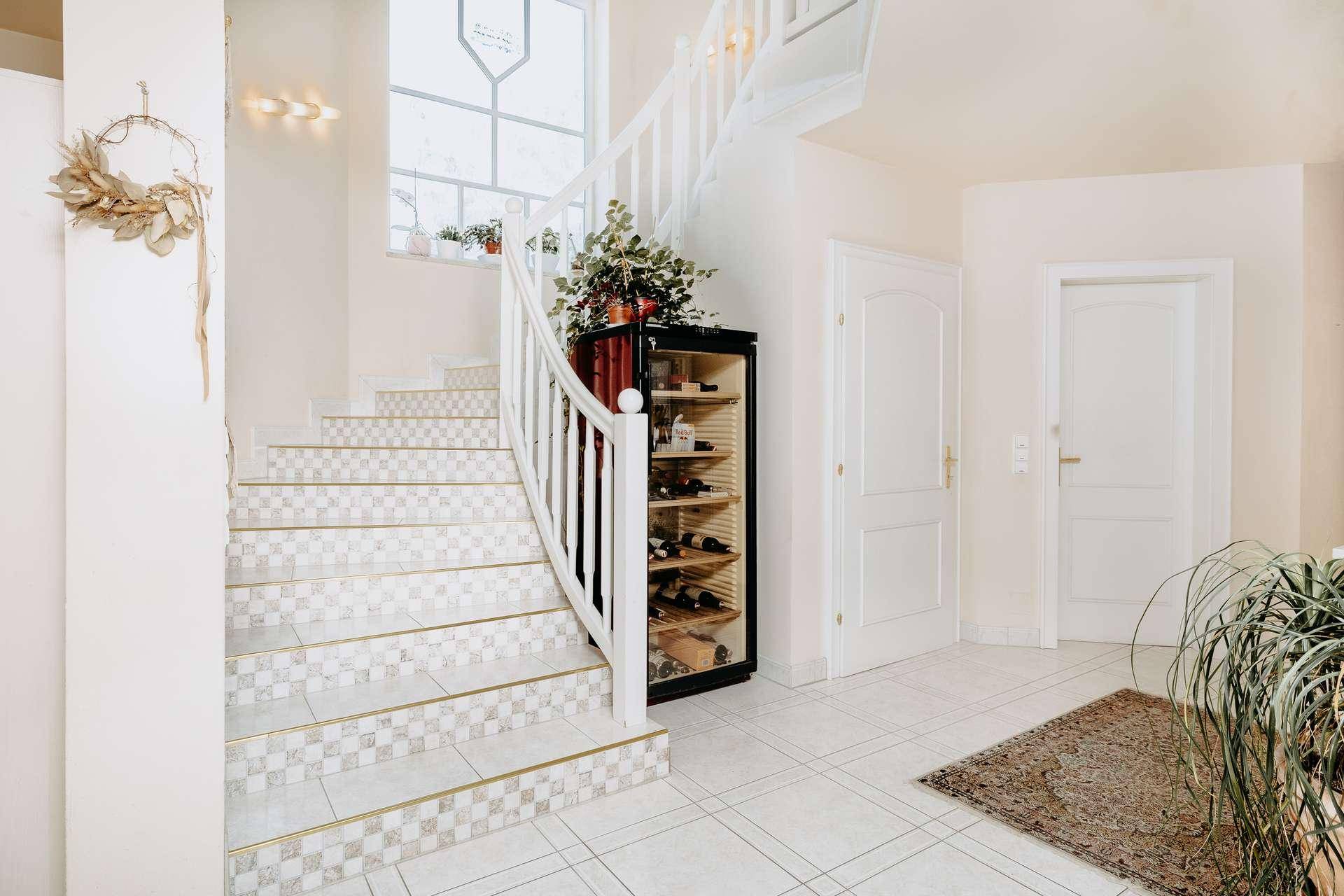 Elegantes Treppenhaus mit geschwungener Treppe, Fliesenboden und integriertem Weinkühlschrank.