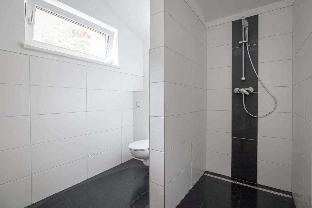 Modernes Badezimmer mit weißen Fliesen, begehbarer Dusche und Dachfenster für natürliches Licht.