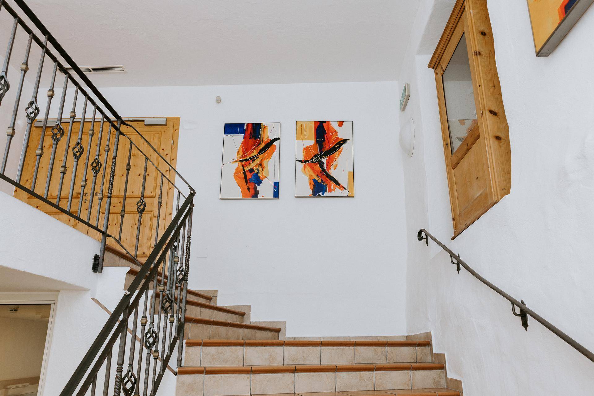 Treppenhaus mit Fliesenstufen, schmiedeeisernem Geländer und modernen Kunstwerken an der Wand.