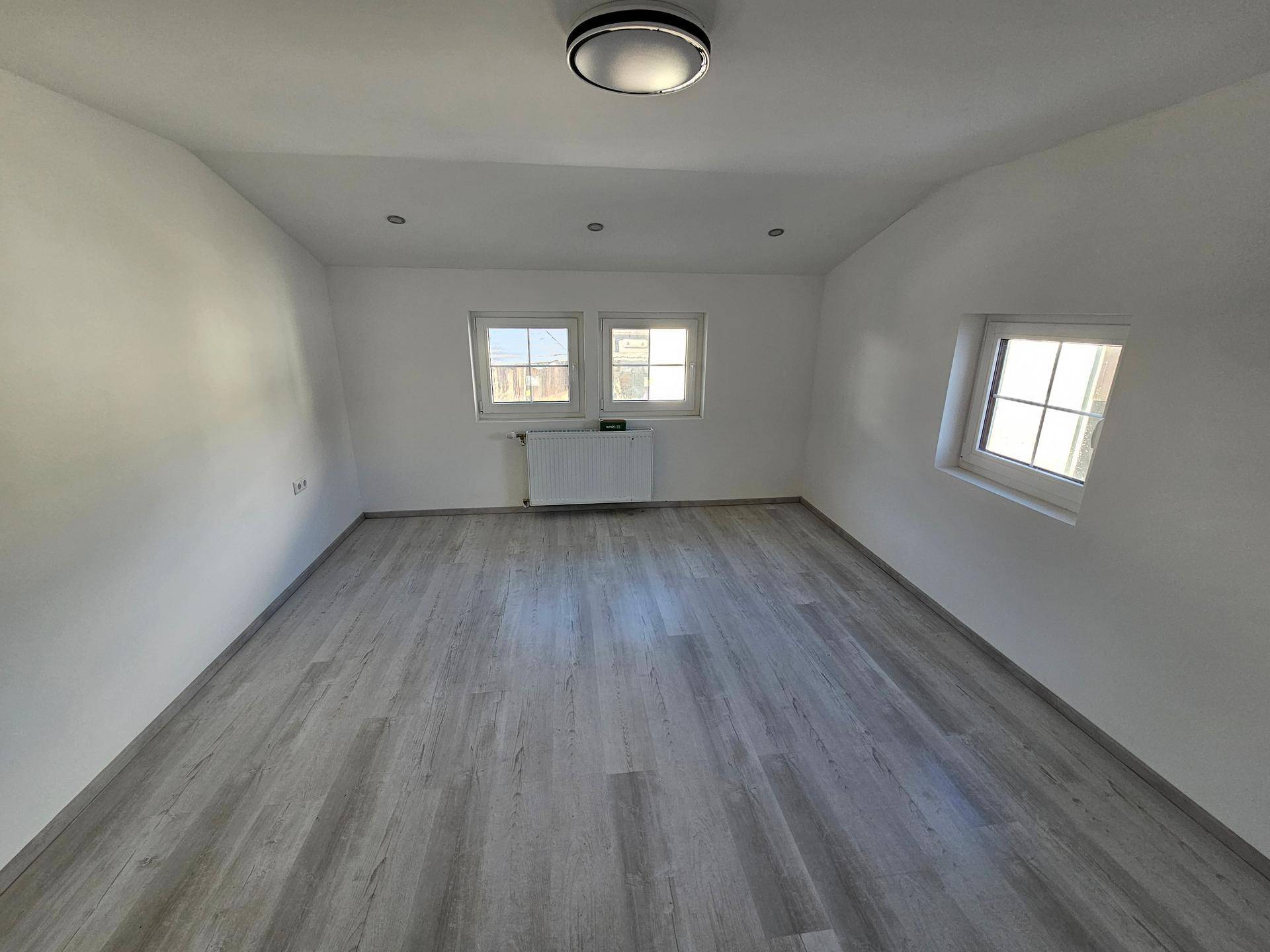 Heller Raum mit modernem Laminatboden, mehreren Fenstern und weiß gestrichenen Wänden.