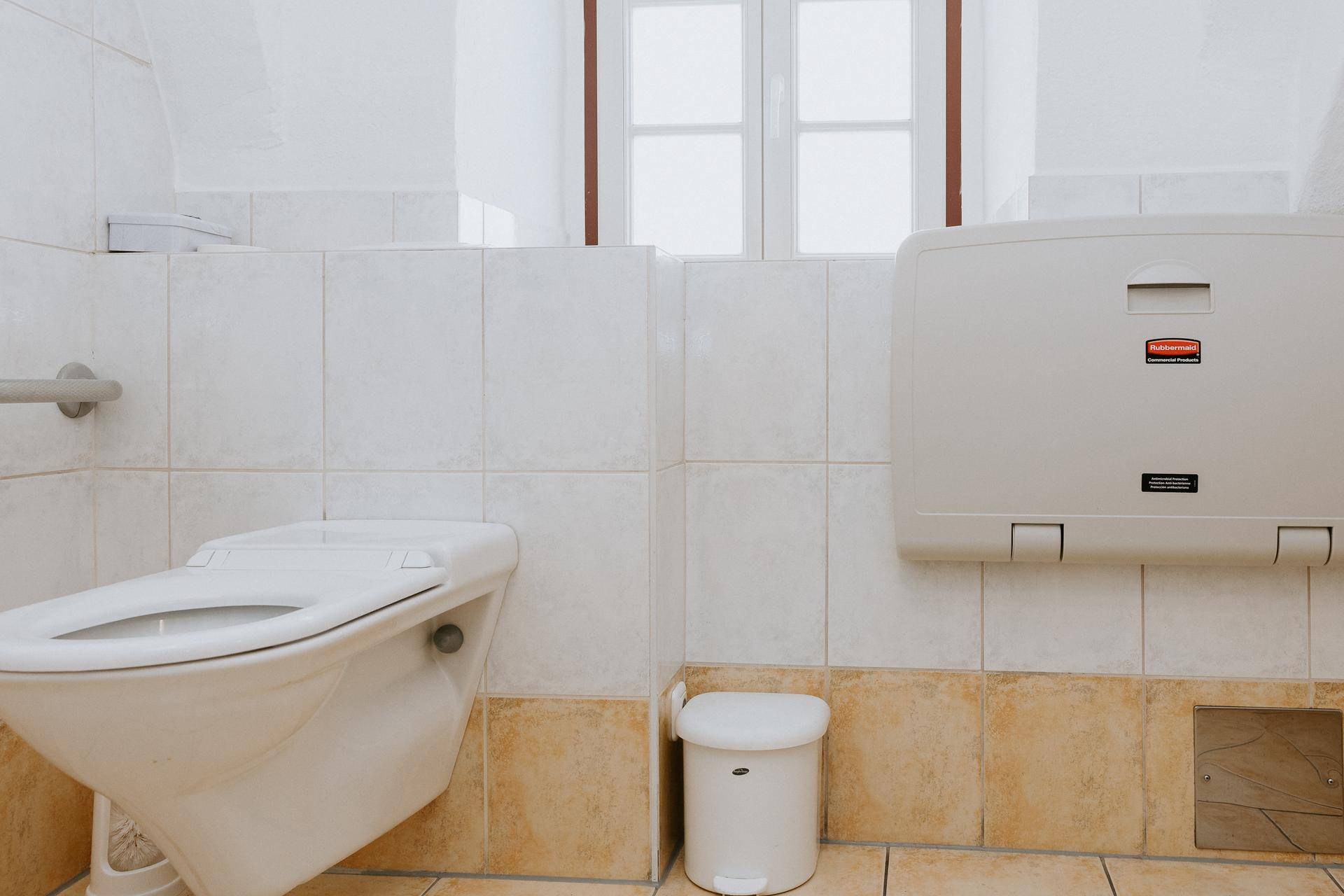 Saubere Toilette mit Wand-WC, Wickeltisch und Fenster für natürliche Belüftung.