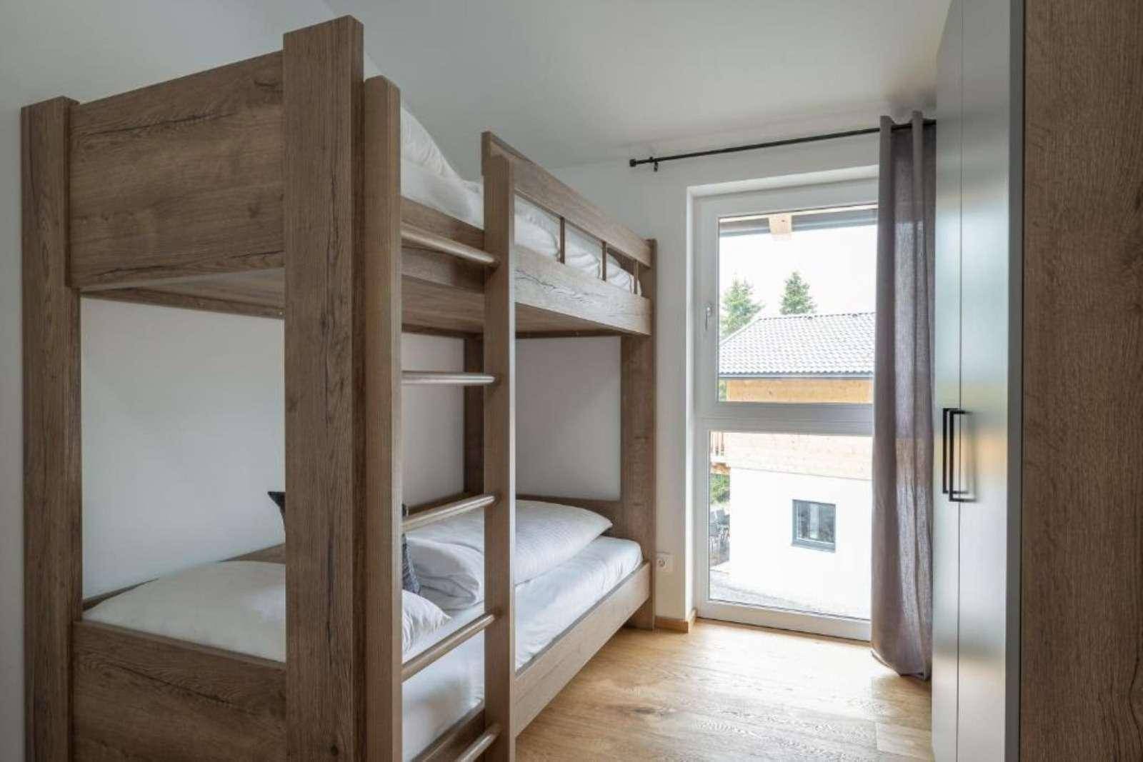 Kinderzimmer mit Etagenbetten aus Holz, Holzboden und einem Fenster für natürliches Licht.
