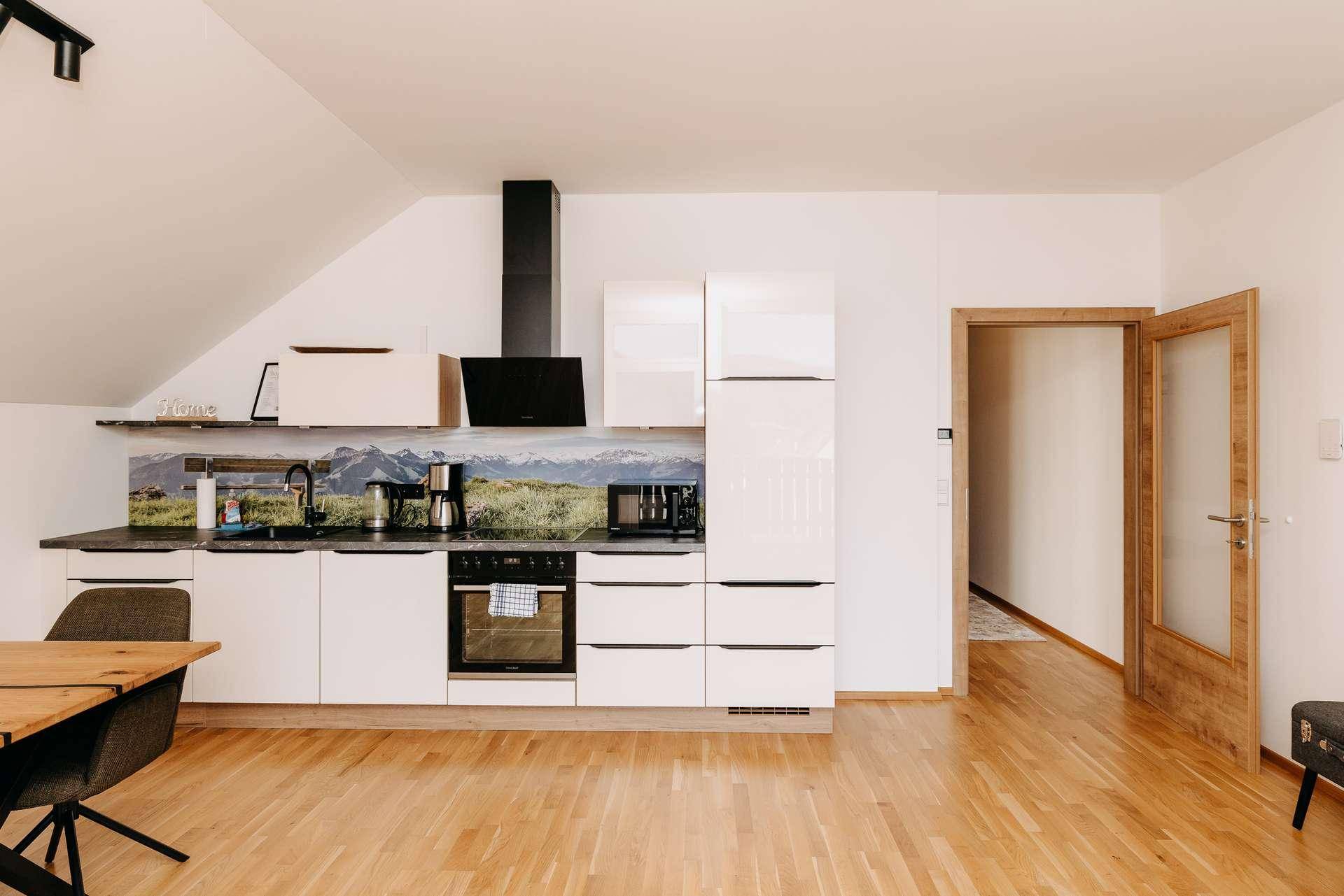 Helle Küche mit modernen weißen Schränken, integrierten Geräten und Holzboden.