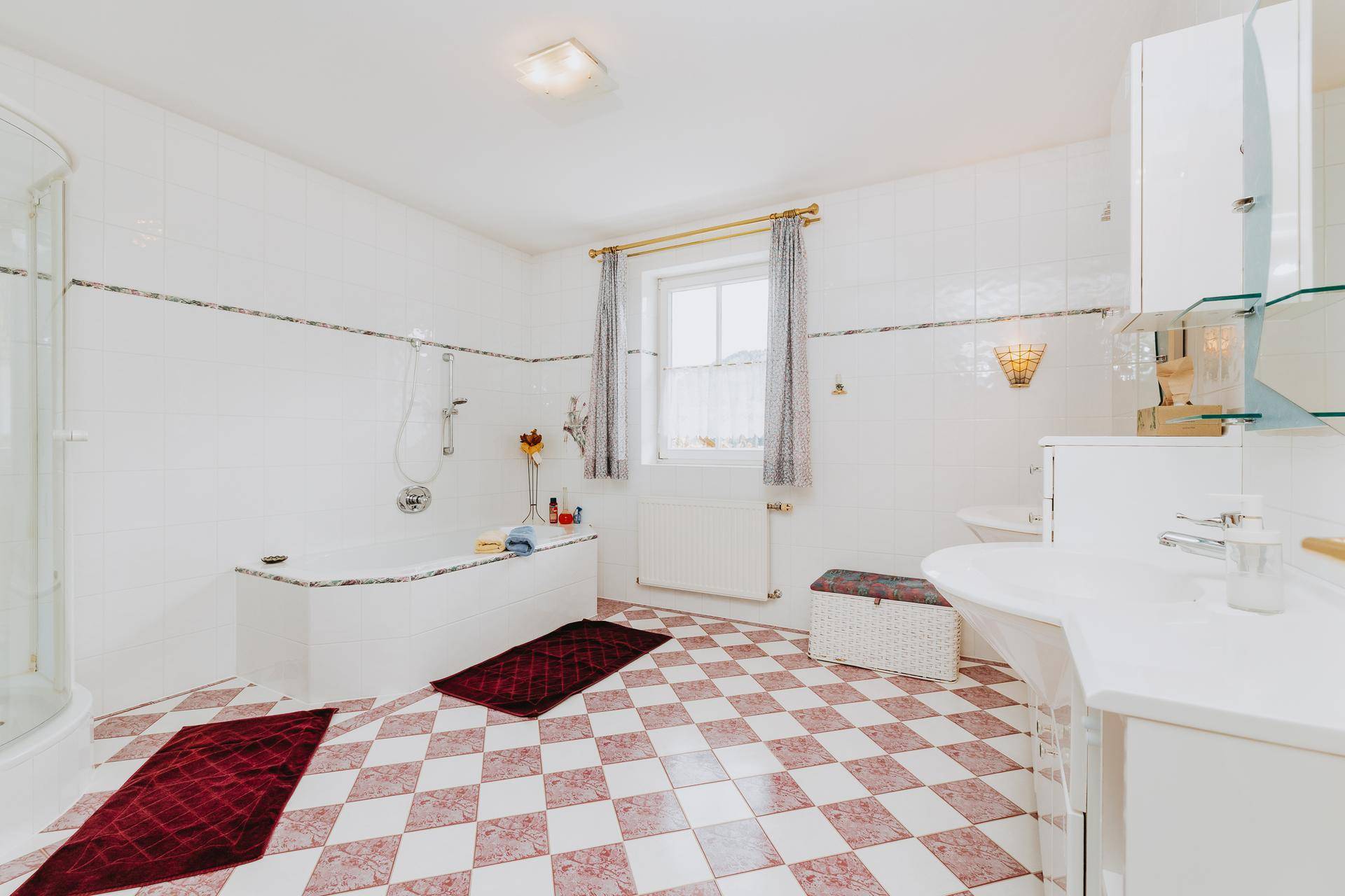 Badezimmer mit Badewanne, Dusche, WC und Fenster, ausgestattet mit rosa-weißem Fliesenboden.