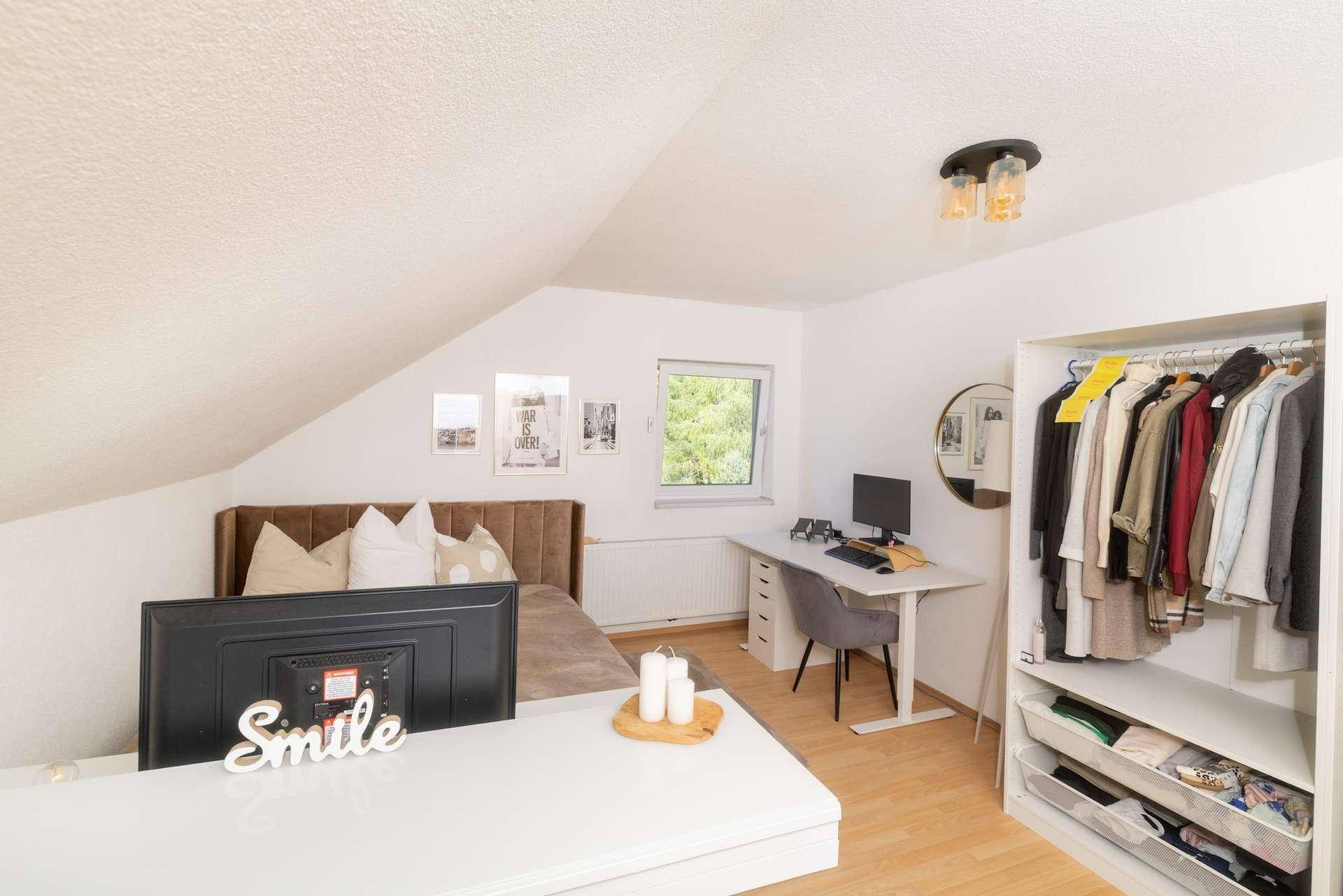Modern eingerichtetes Schlafzimmer mit Bett, Schreibtisch und offenem Kleiderschrank.