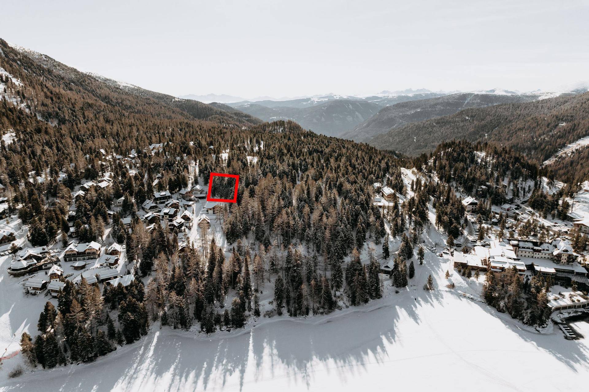 Luftaufnahme einer verschneiten Waldlandschaft mit Häusern und einem zugefrorenen See, mit Markierung.