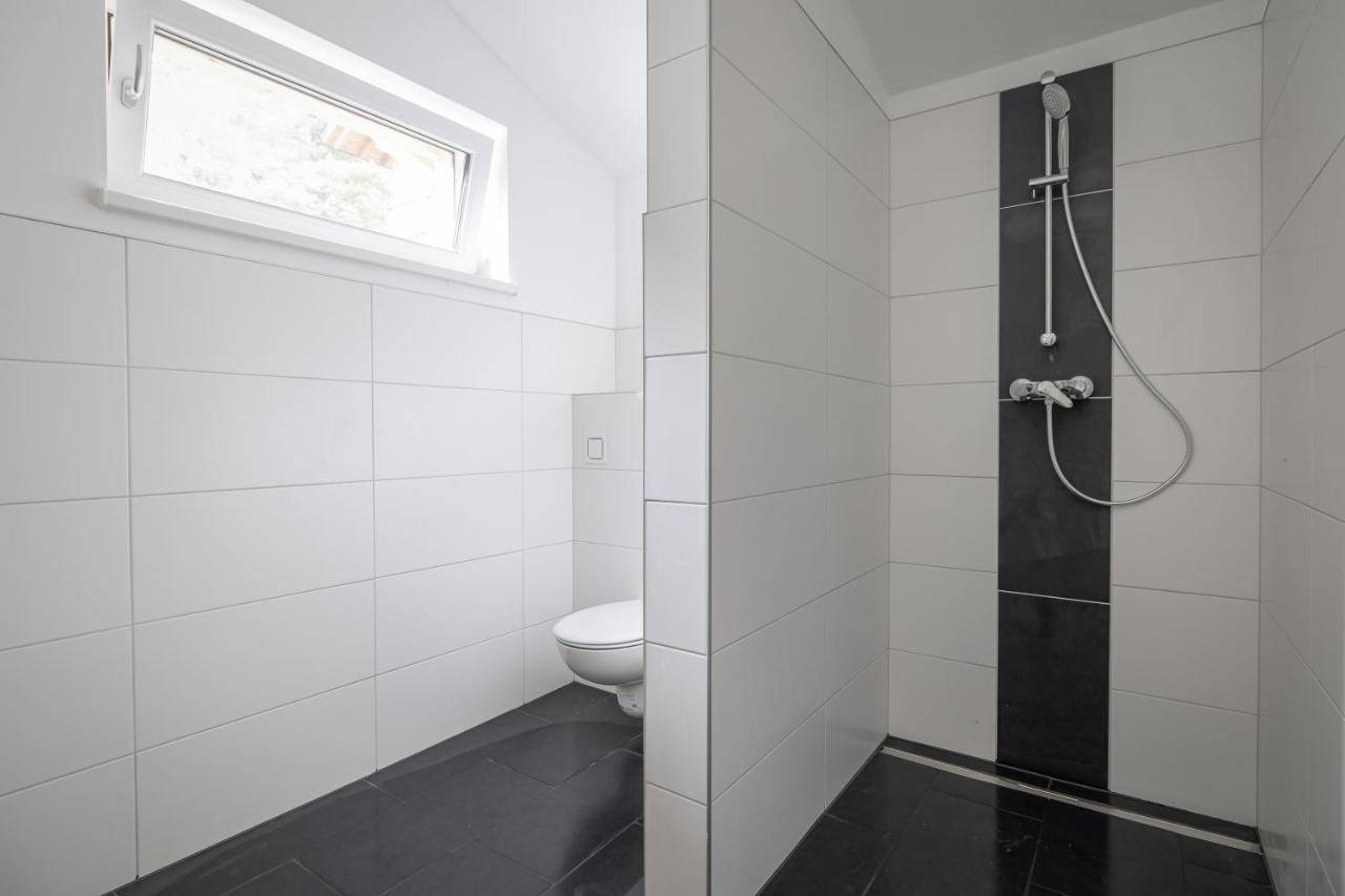 Modernes Badezimmer mit ebenerdiger Dusche, WC und Fenster.