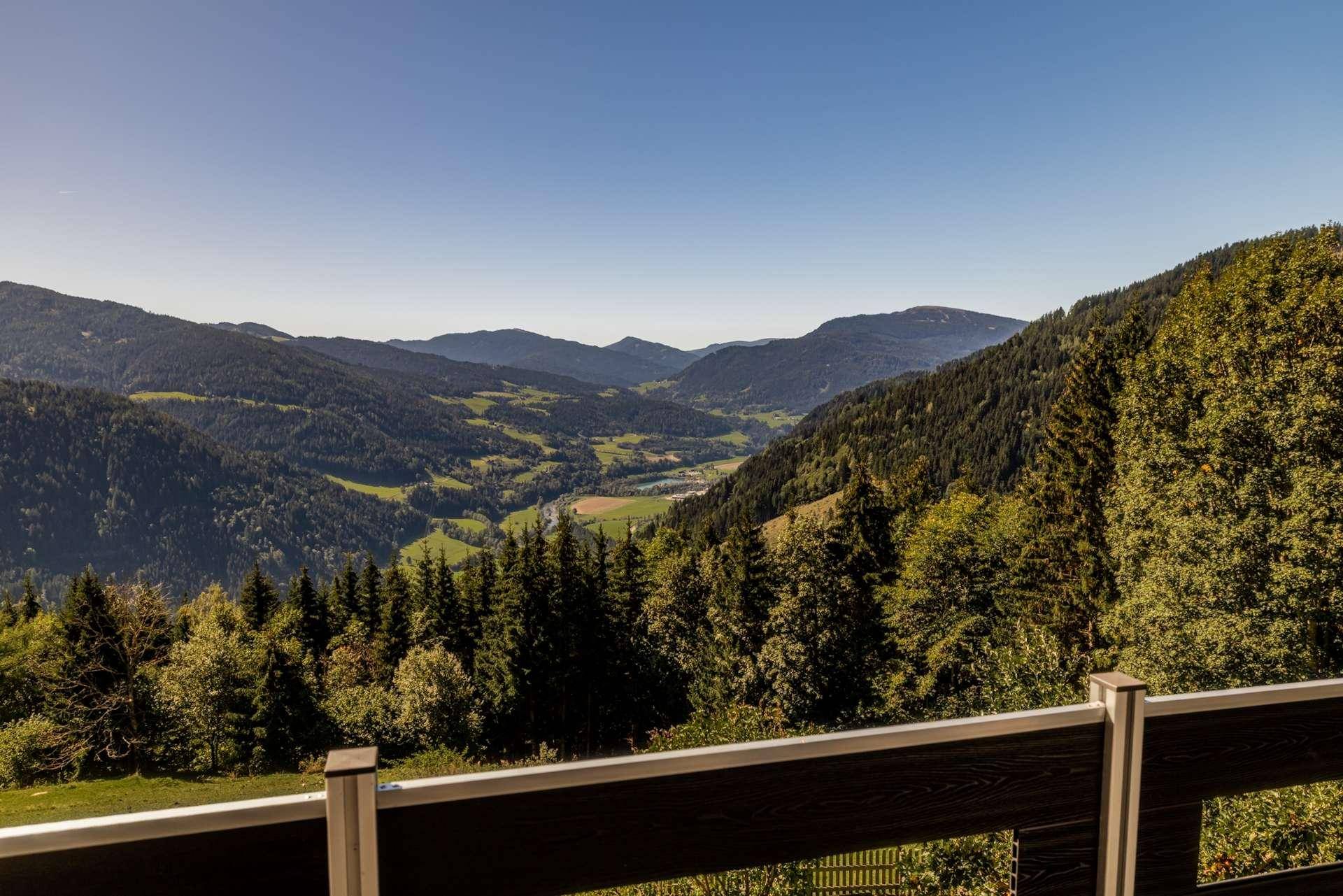 Weitläufiger Blick von einem Balkon über ein grünes Tal mit dichten Wäldern und Bergen.