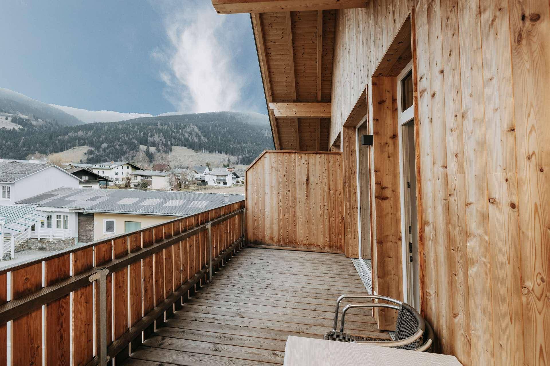 Langer Holzbalkon mit Holzverkleidung und Panoramablick auf die umliegenden Berge und die Natur.