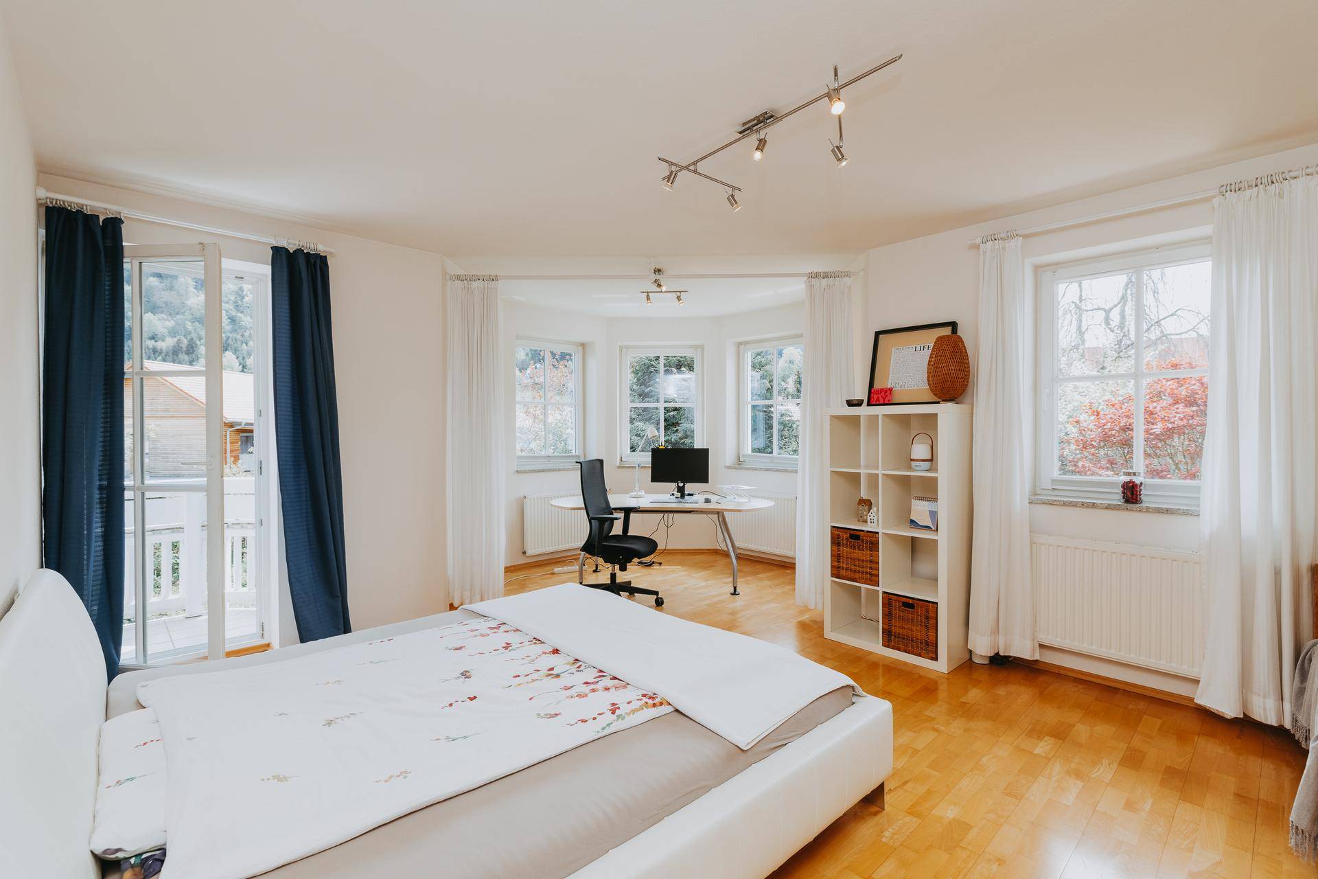 Schlafzimmer mit Doppelbett, Schreibtisch und Zugang zu einem kleinen Balkon.