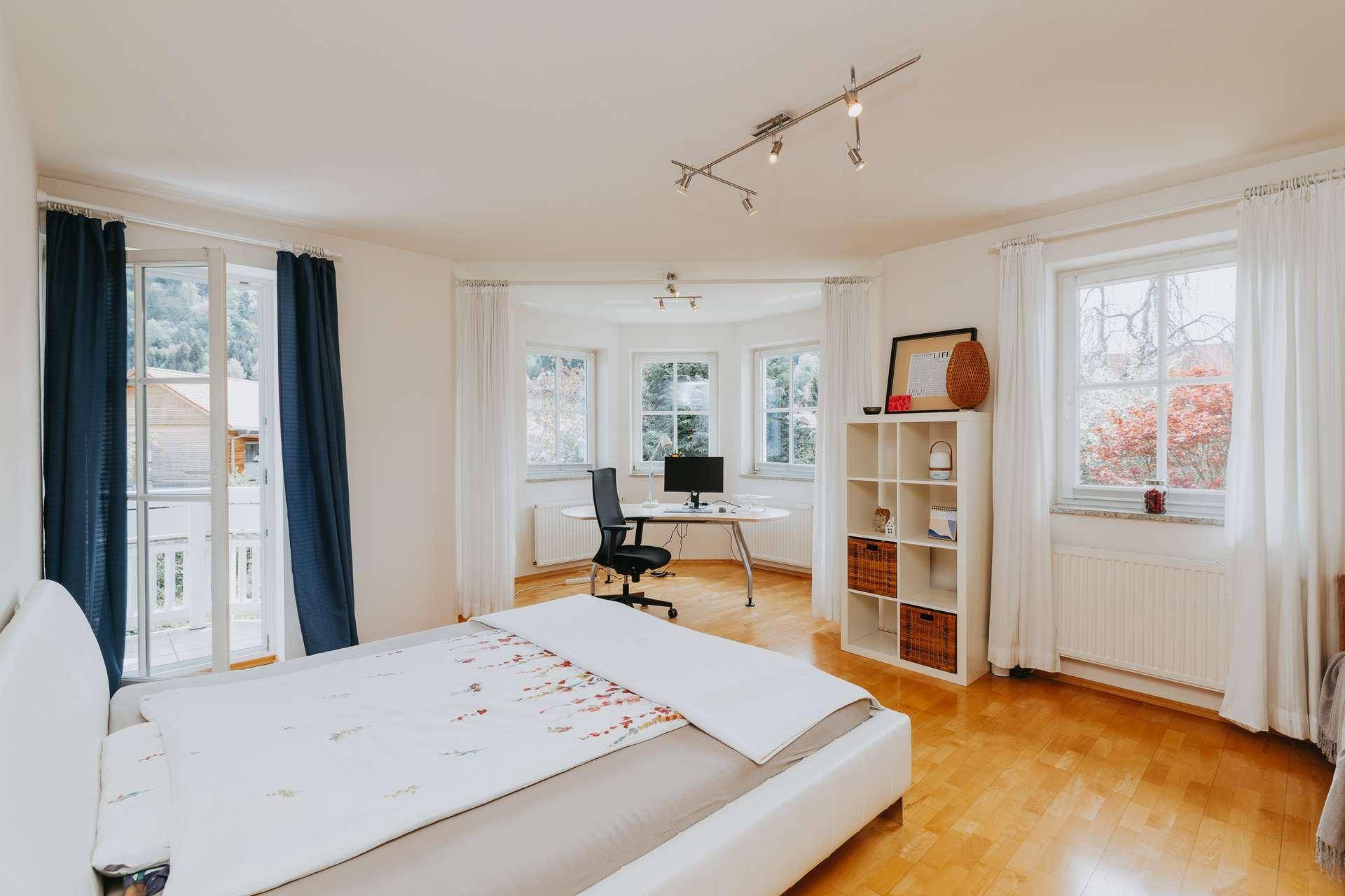 Schlafzimmer mit Holzboden, Doppelbett und einem integrierten Arbeitsbereich am Fenster.